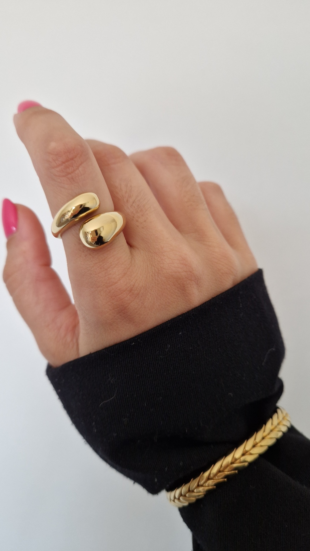 Mão com anel dourado aberto e pulseira trançada dourada sobre manga preta