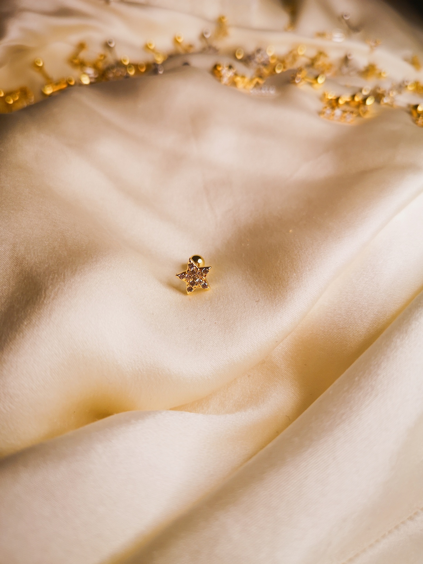 Brinco em forma de estrela sobre tecido creme com franjas douradas ao fundo