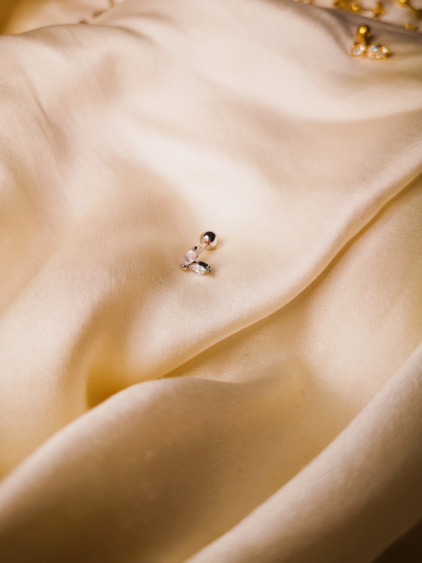 Brinco de aço com pedras brilhantes sobre tecido creme.