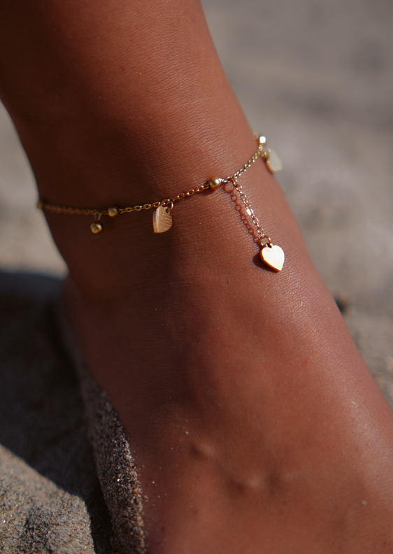 Torna tornozelo dourado com pendentes em forma de coração e círculo na areia