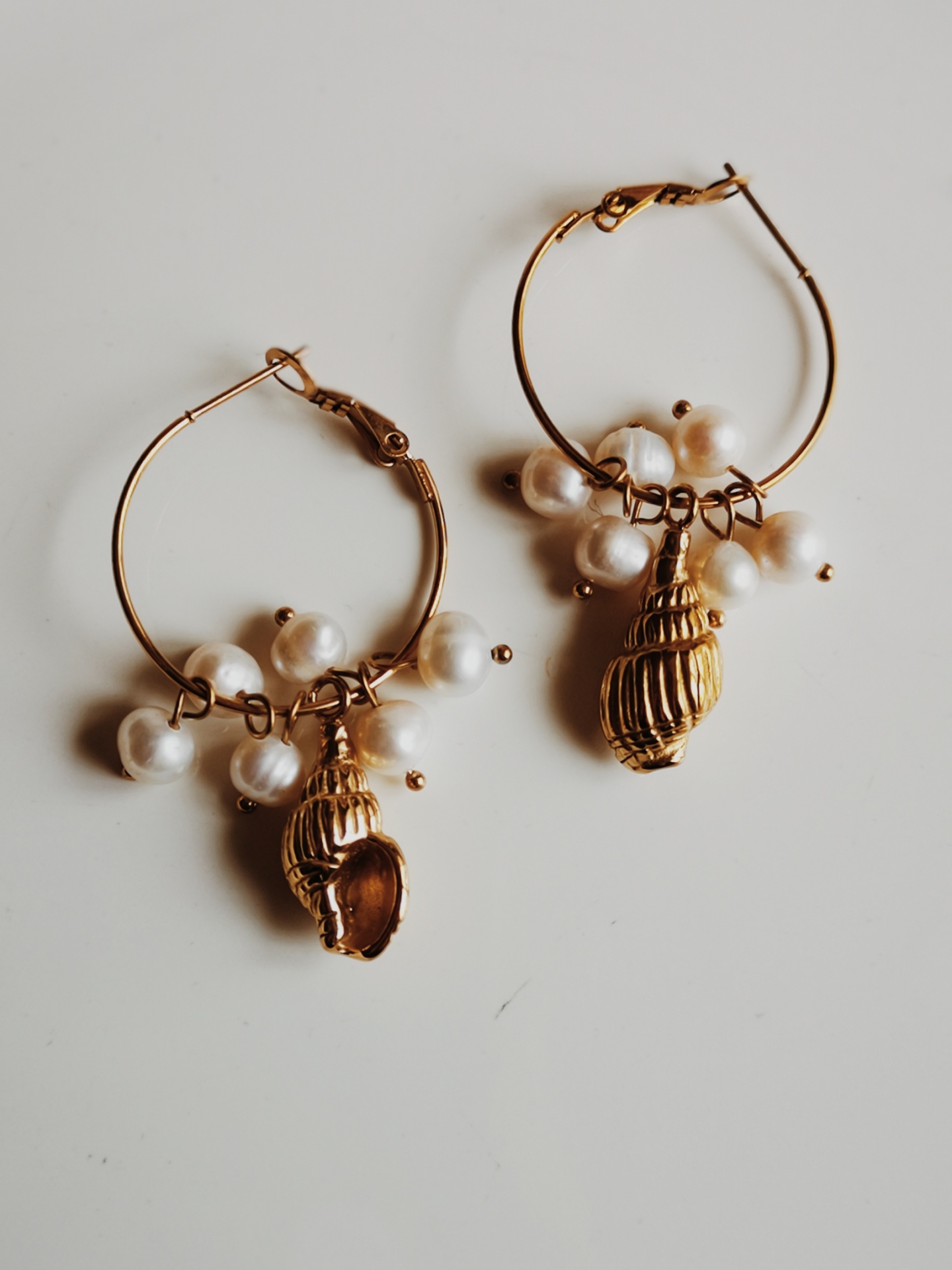Brincos dourados com conchas e pérolas sobre fundo branco