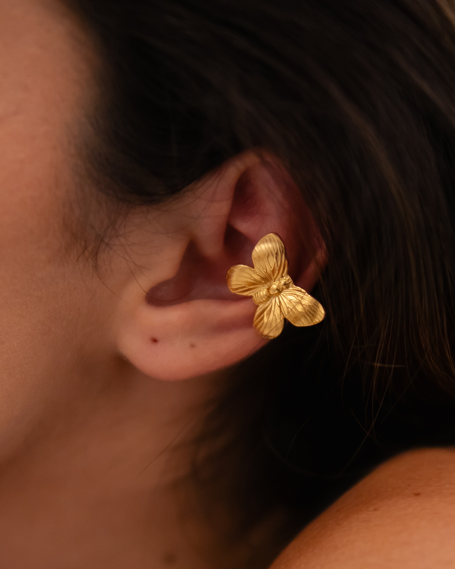 Brinco dourado em forma de borboleta na orelha de uma pessoa