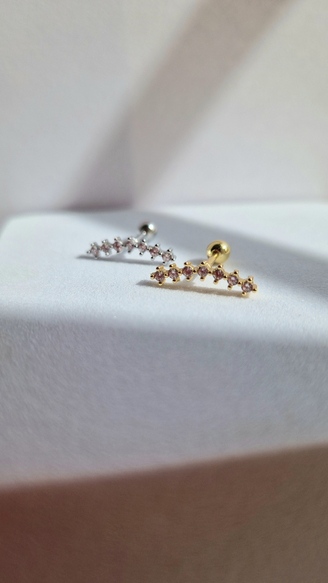 Brincos pequenos dourado e prateado com pedras transparentes em superfície branca