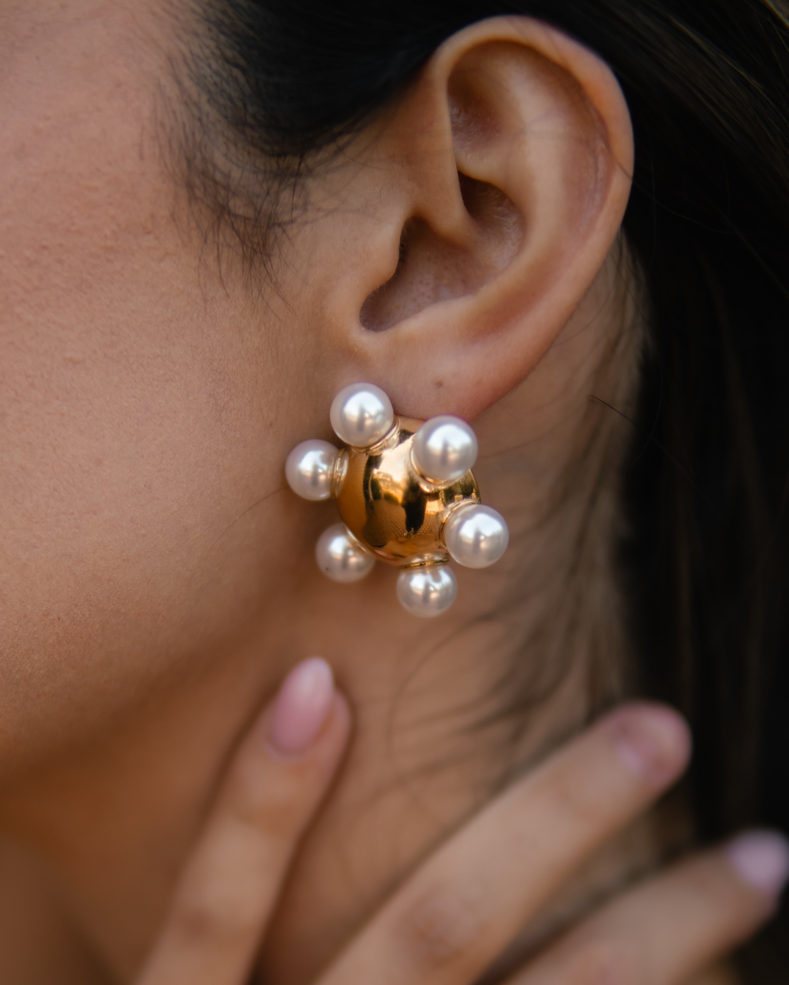 Brinco dourado com pérolas brancas na orelha