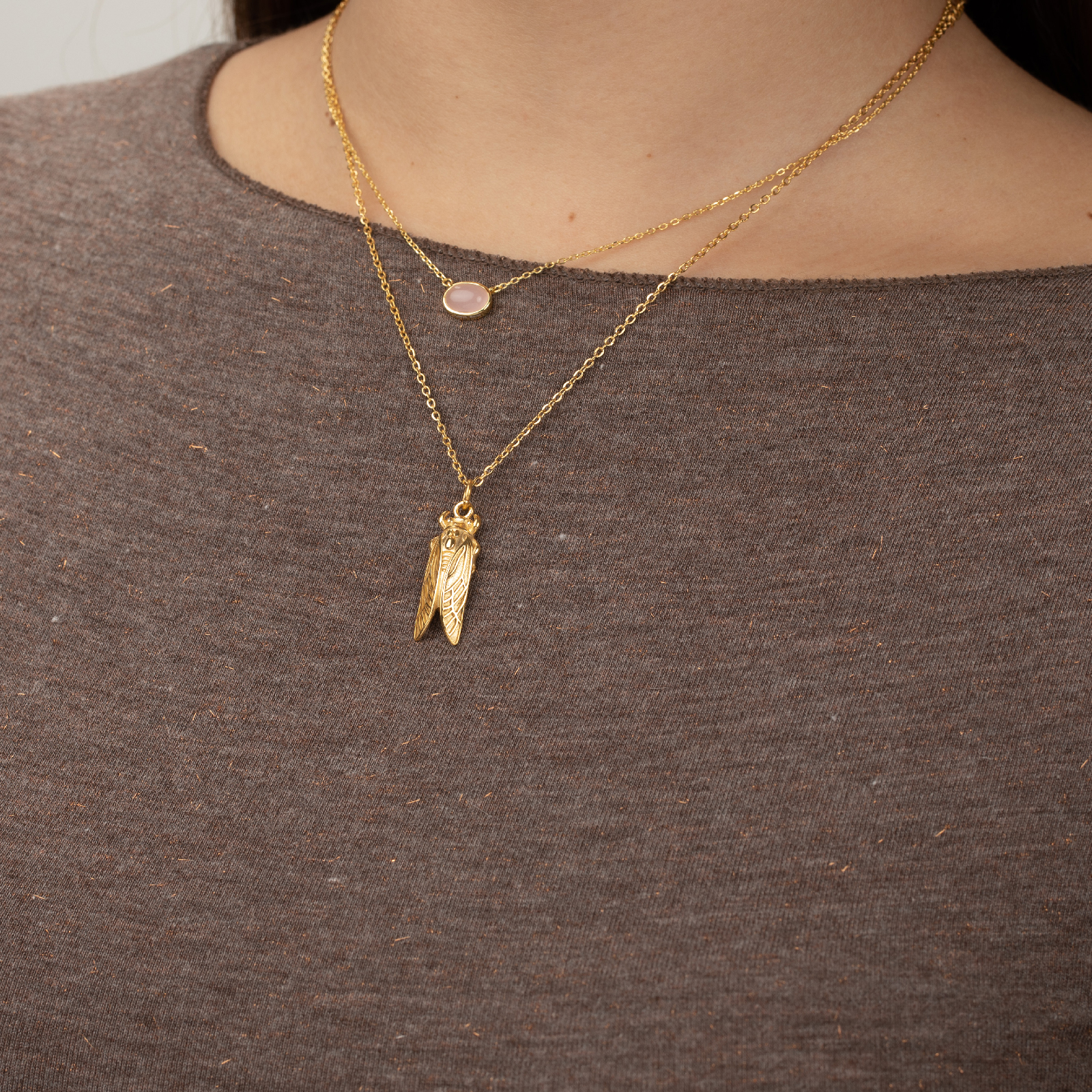 Colares dourados com pingentes usados por pessoa com camisola castanha