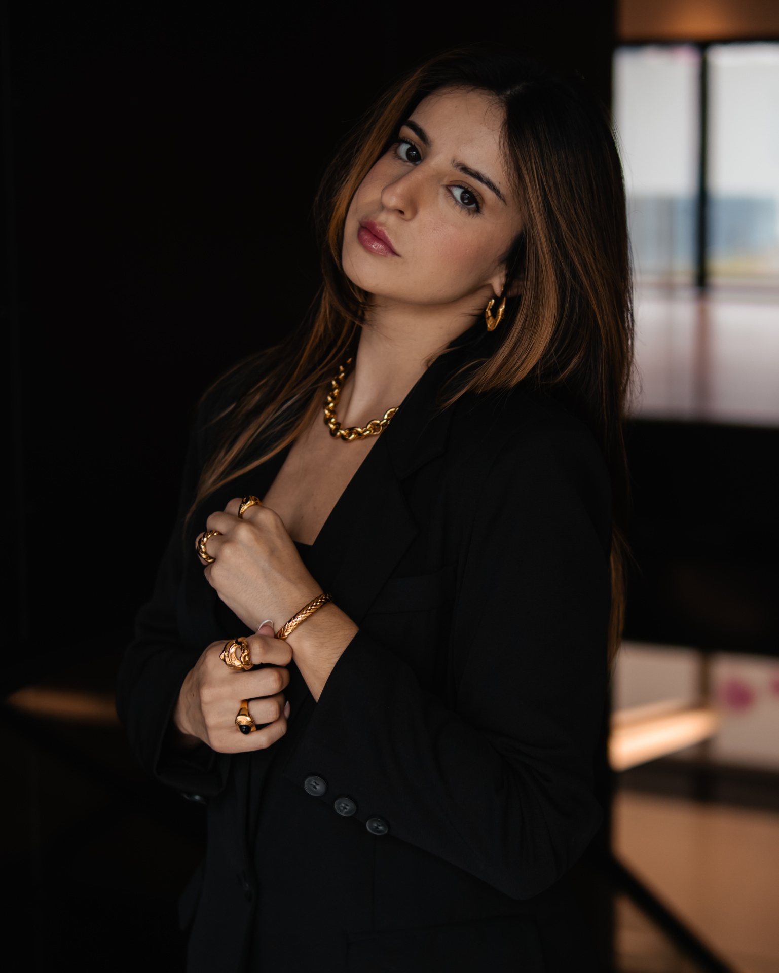 Mulher com casaco preto e joias douradas, em ambiente interior