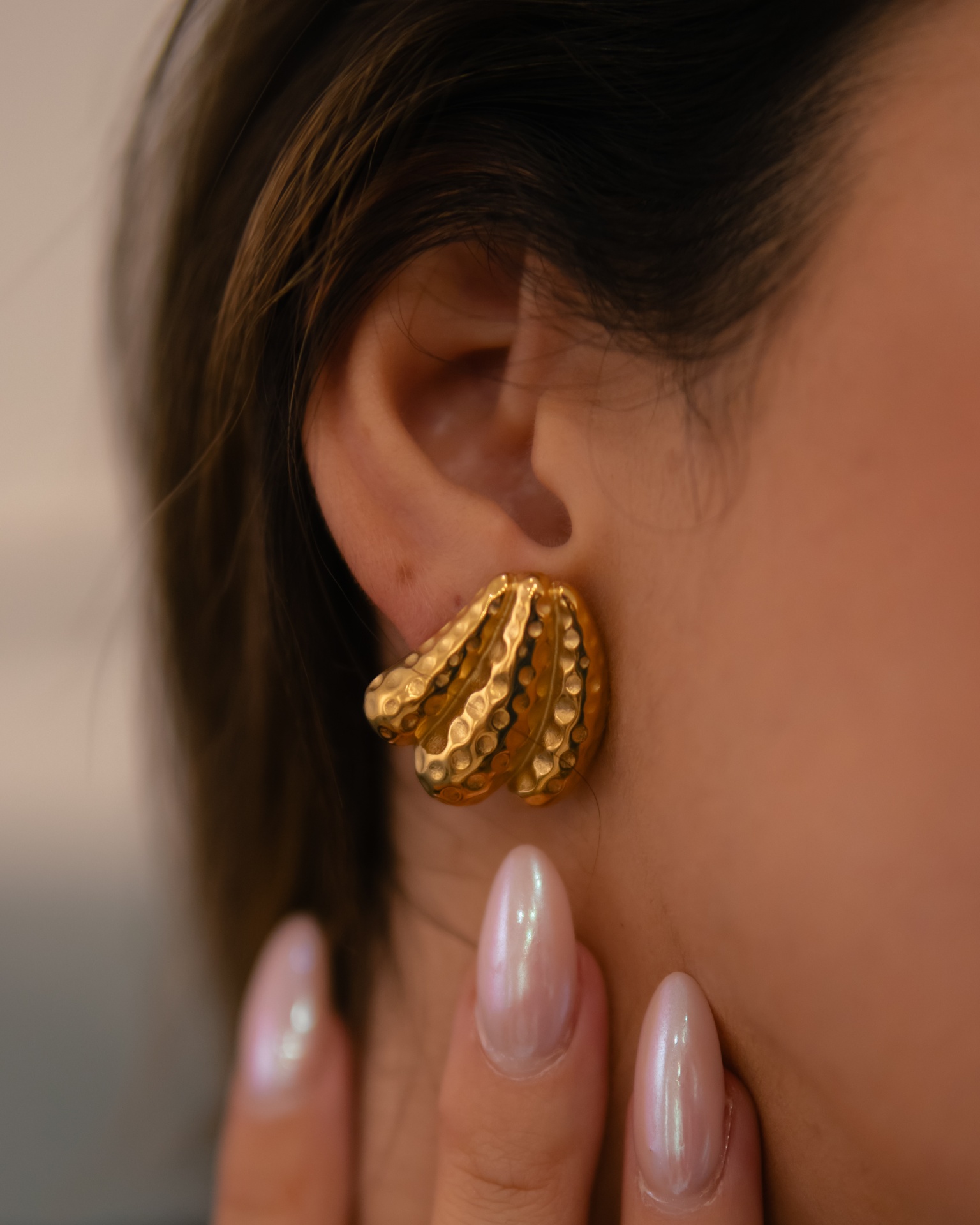 Brinco dourado texturizado tipo leque na orelha de mulher com unhas peroladas