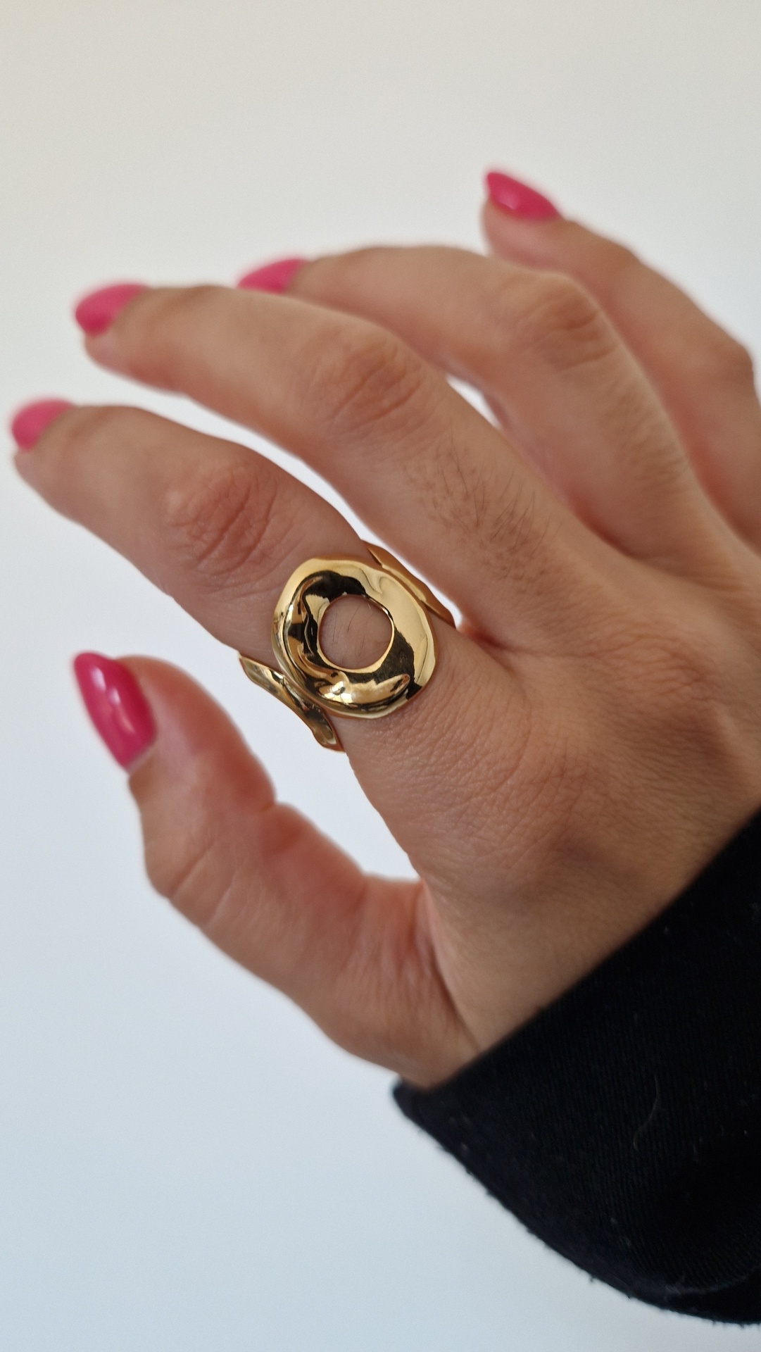 Anel dourado circular em dedo de mão com unhas rosas