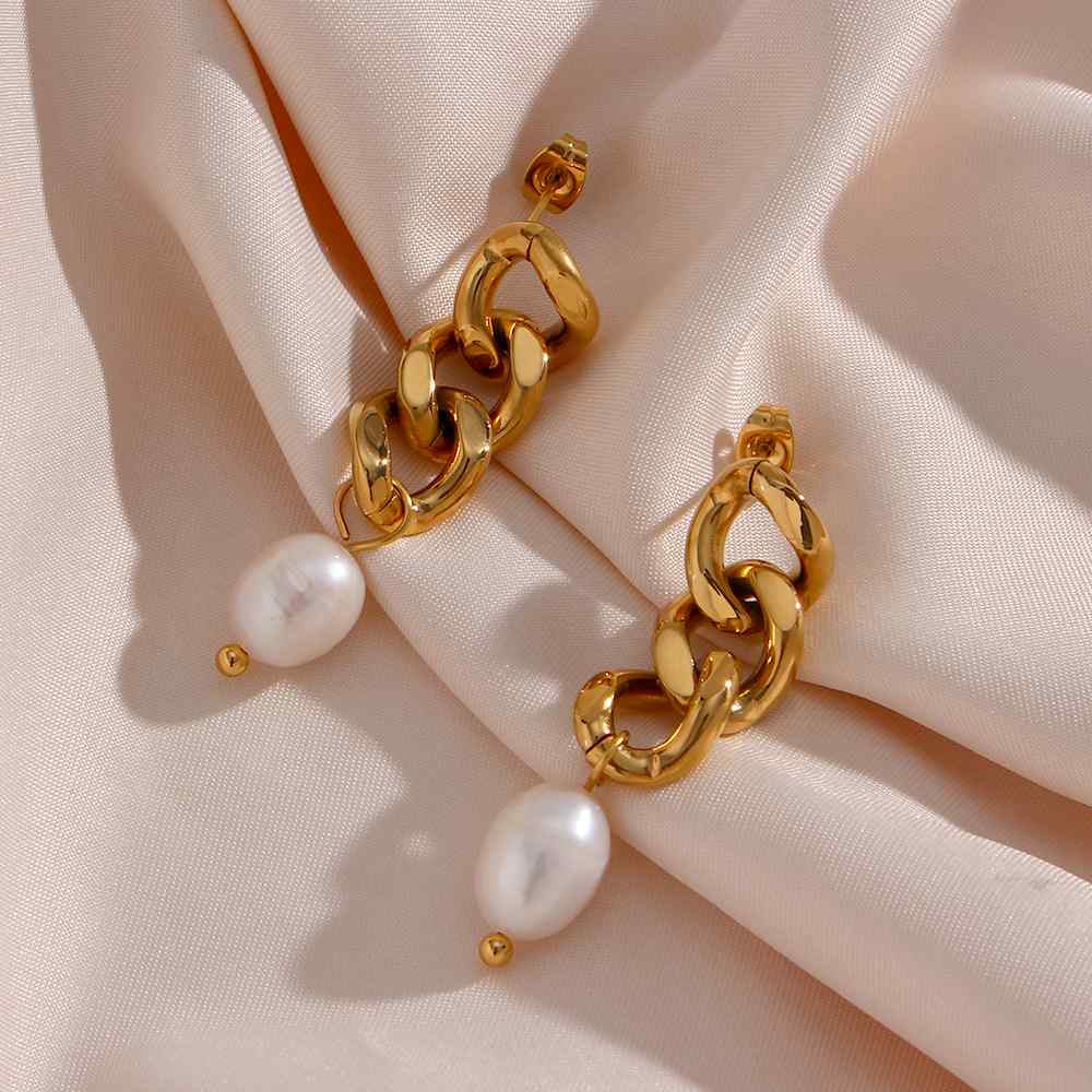 Brincos dourados com pérola pendurada sobre tecido rosa de cetim