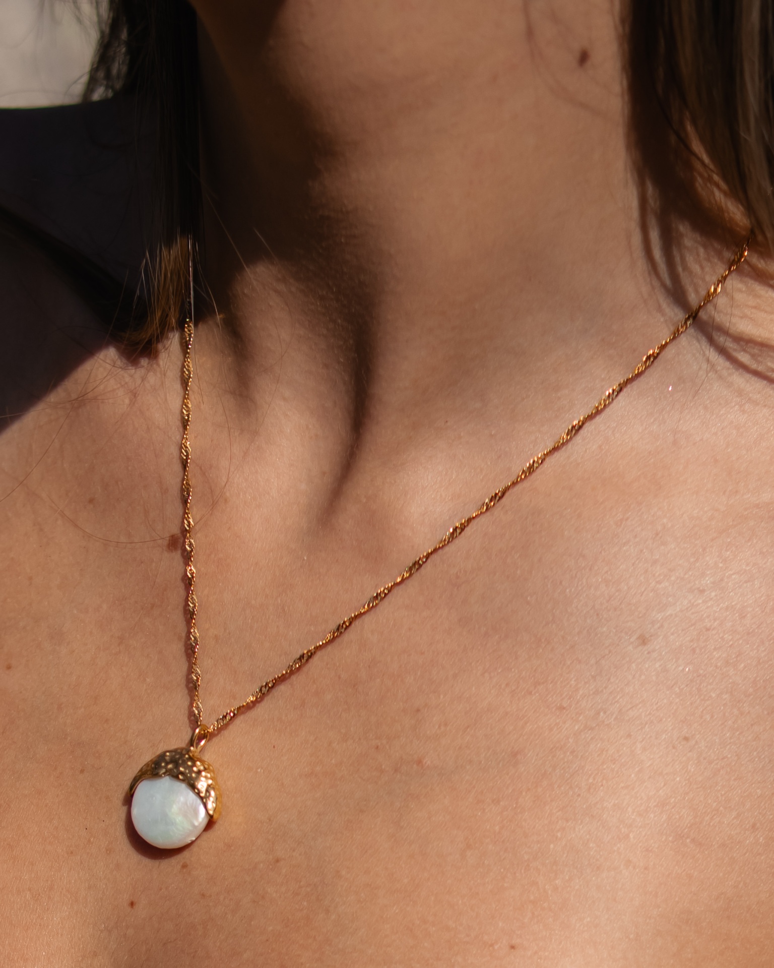 Colar dourado com pendente redondo de pedra branca no pescoço