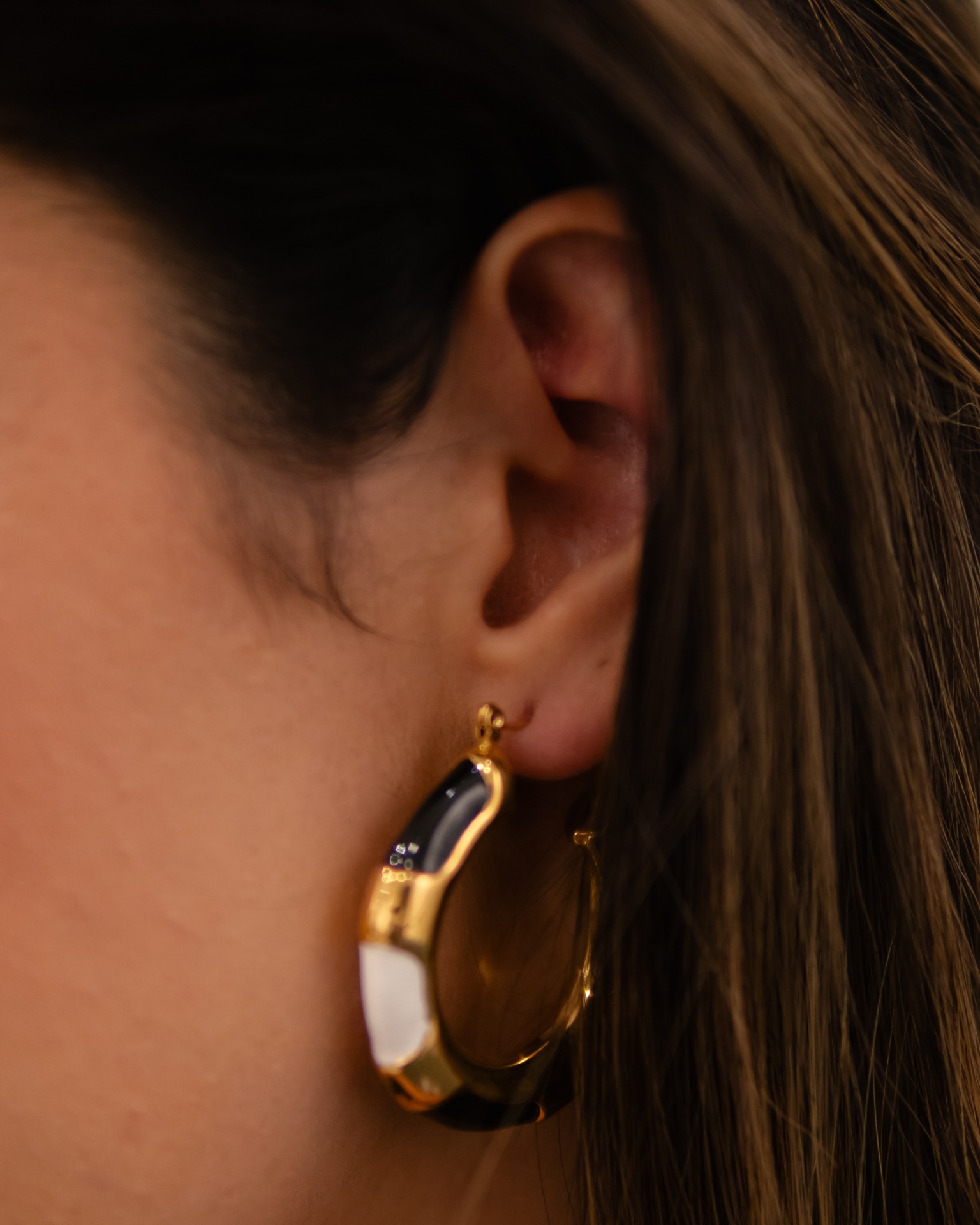 Brinco de argola dourado com detalhes em preto e branco na orelha de uma pessoa