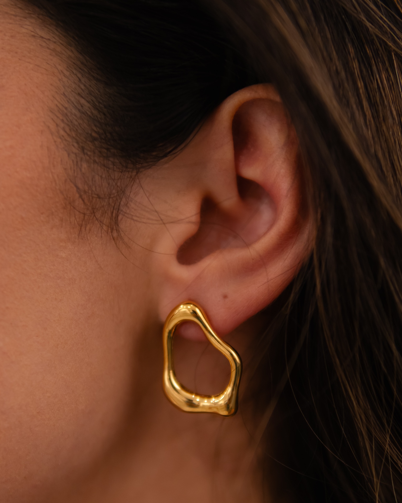 Brinco dourado orgânico na orelha de mulher