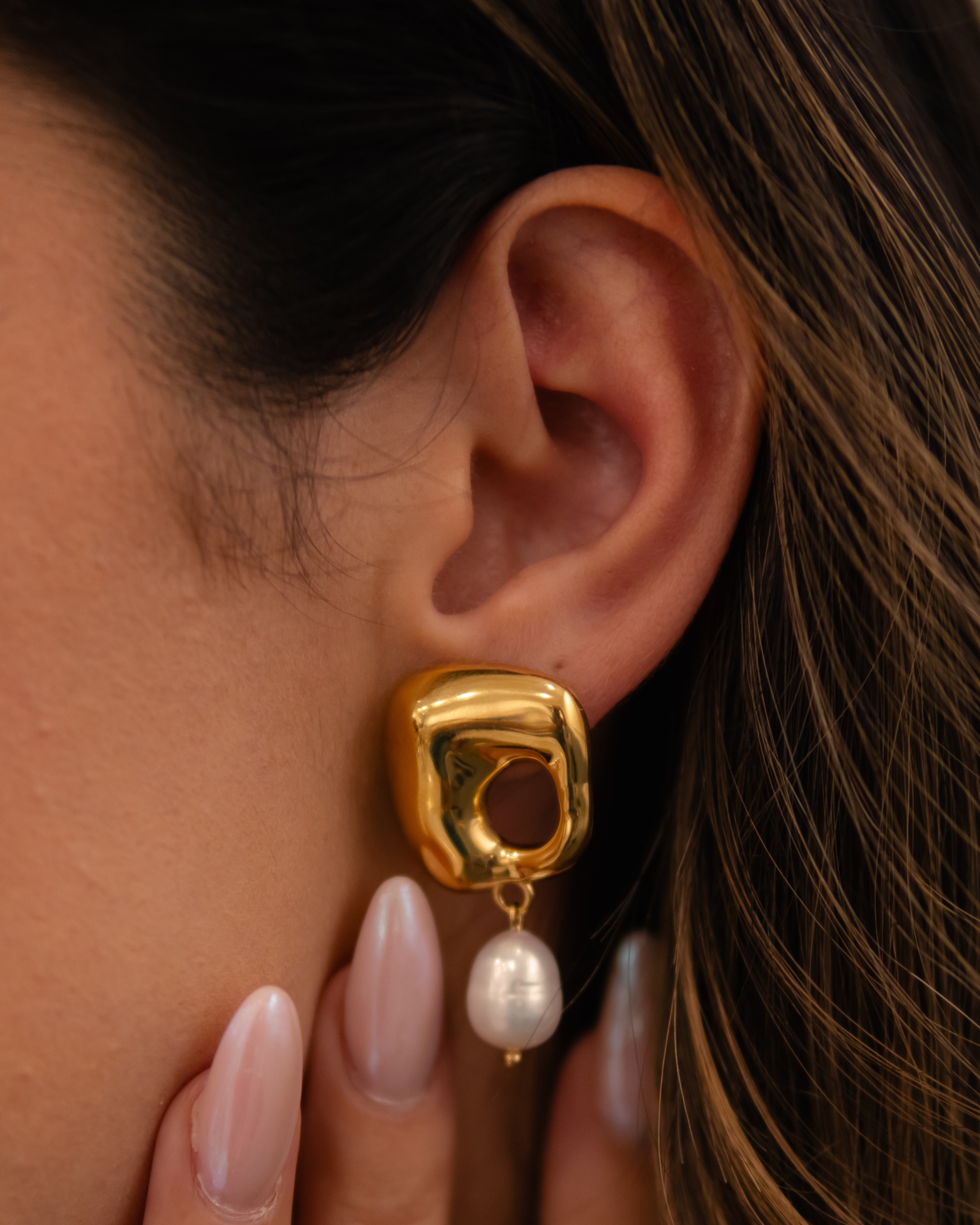 Brinco dourado com pérola pendente numa orelha feminina