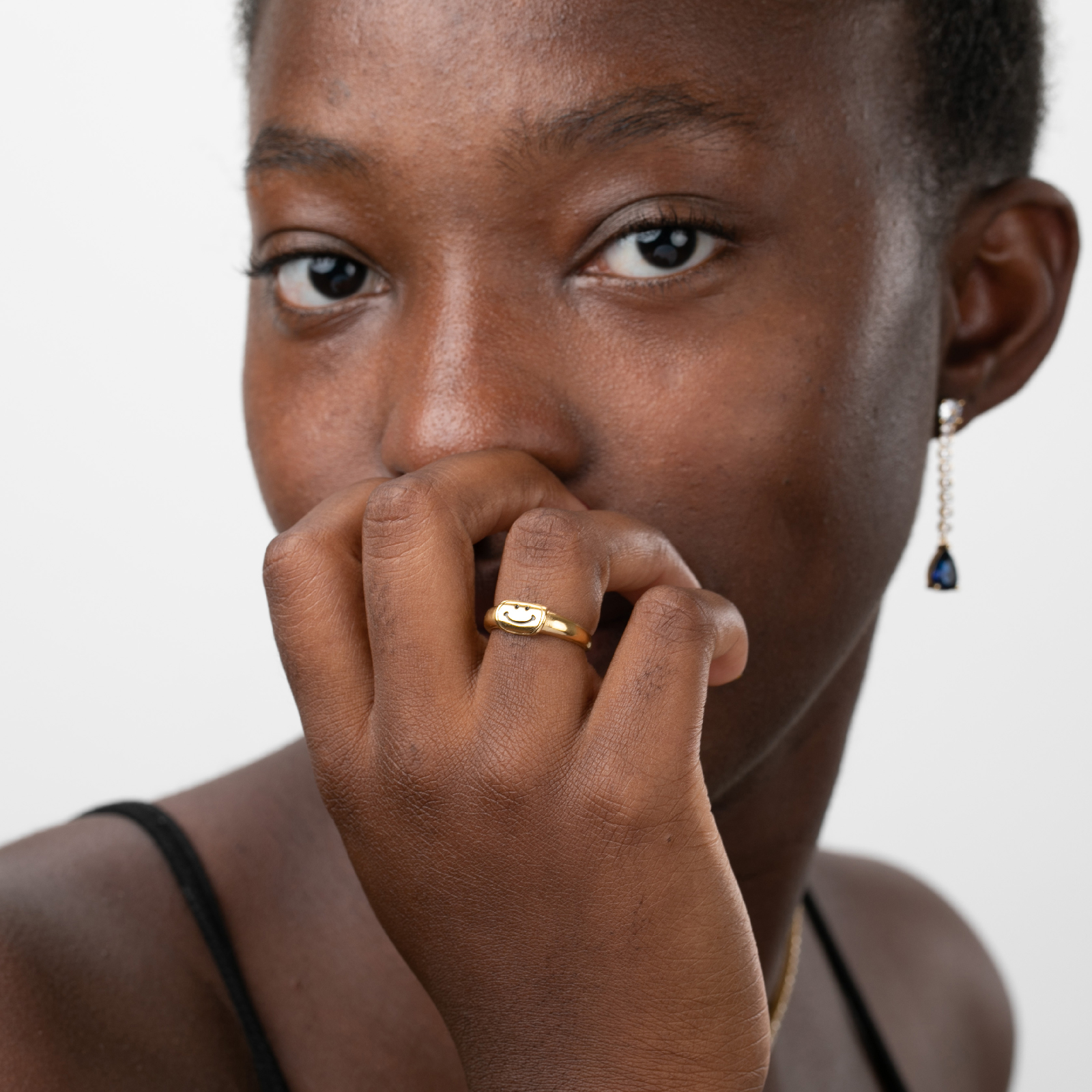 Mulher a usar anel dourado em formato de nó e brincos com pedras azuis