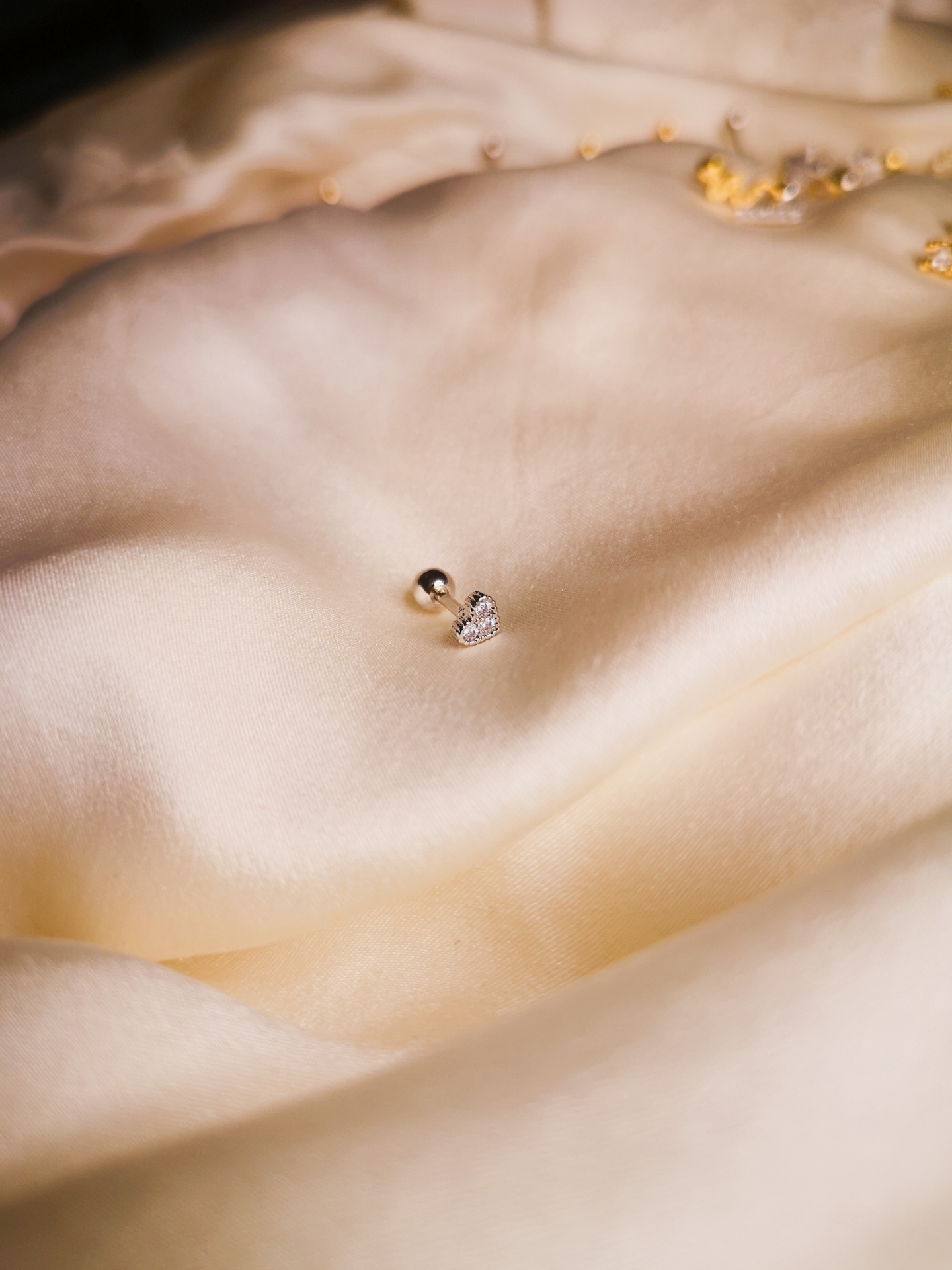 Brinco pequeno em forma de coração sobre tecido de seda creme