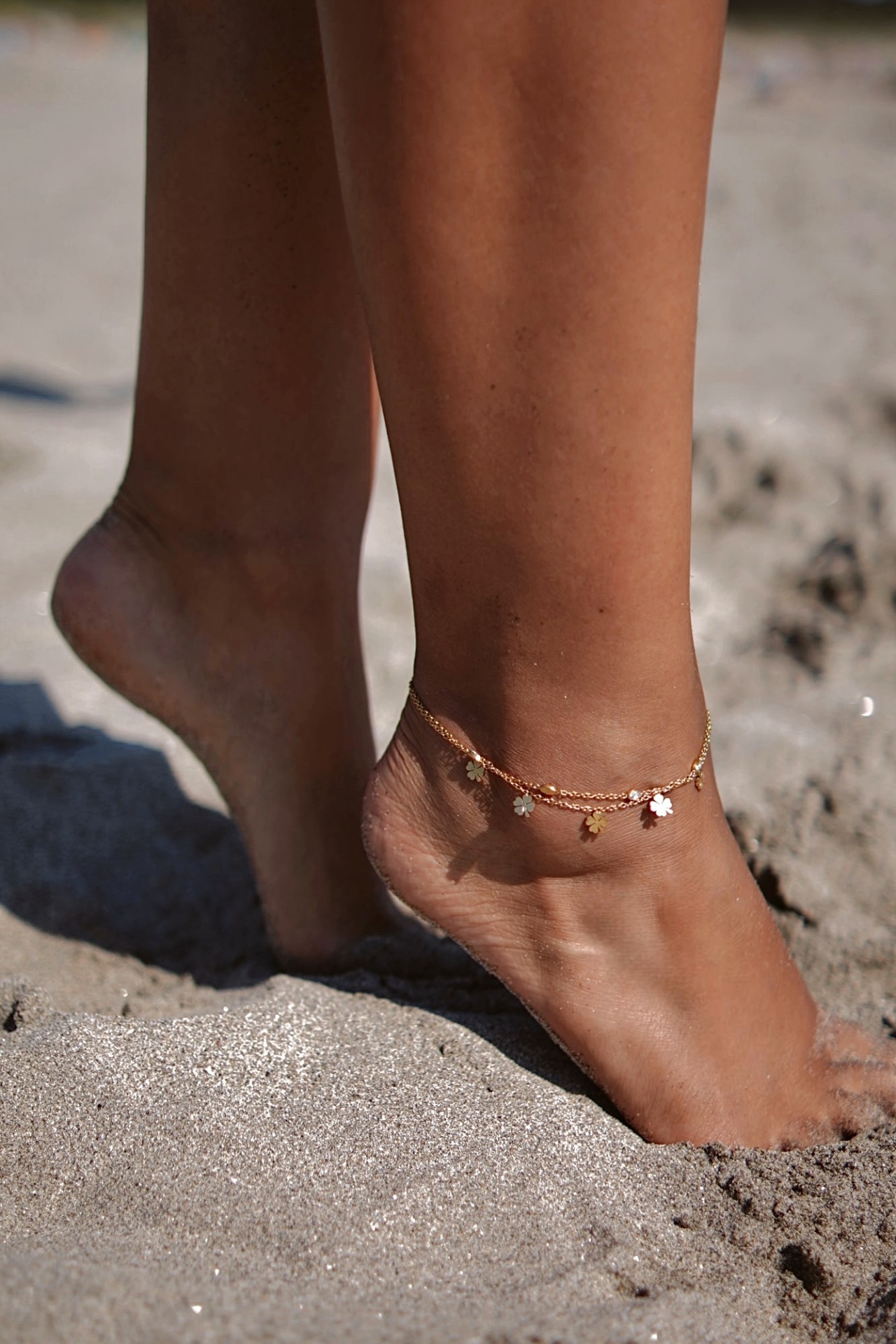 Tornozeleira dourada com pendentes florais no pé na areia