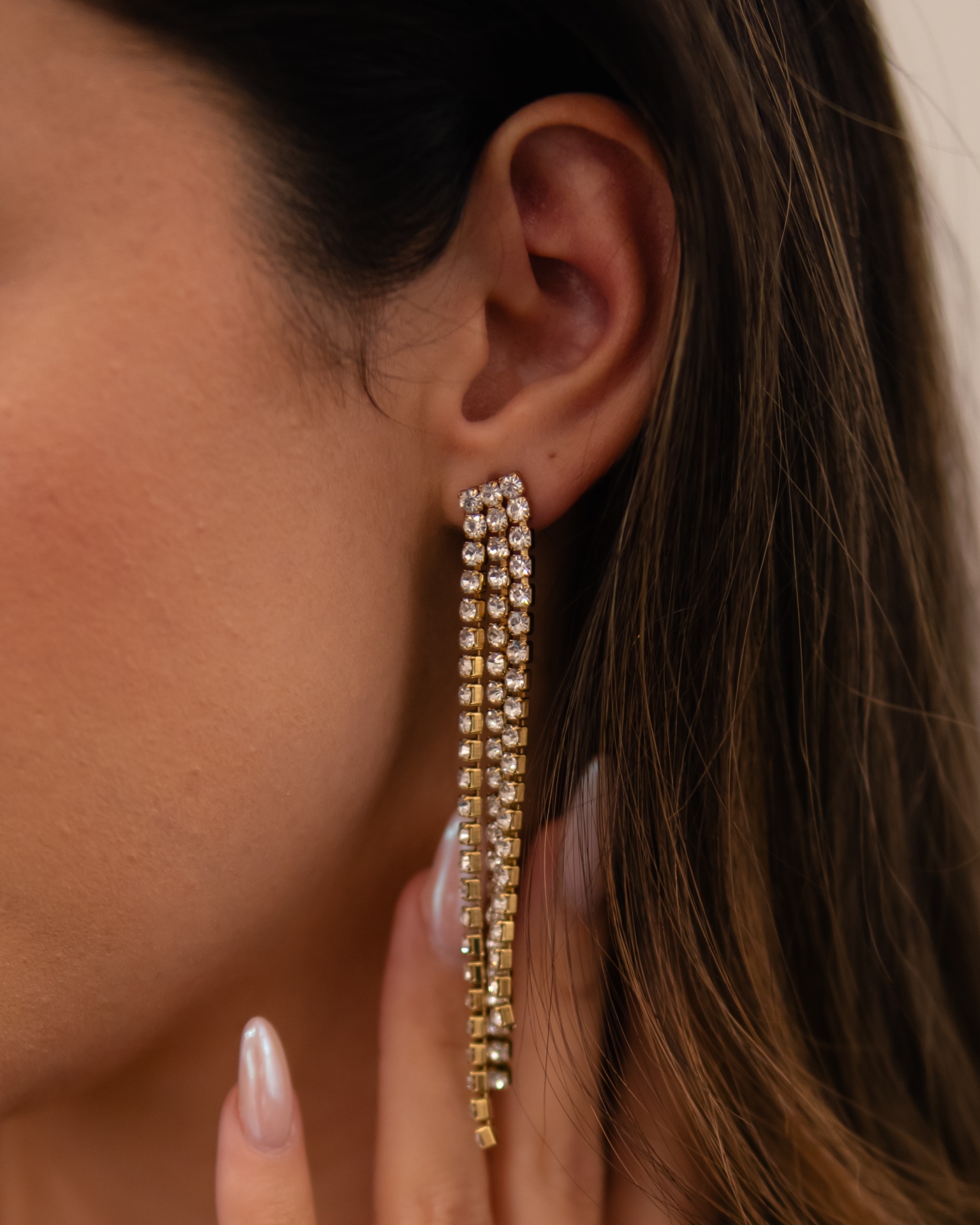 Brincos dourados pendentes com pedras brilhantes em orelha feminina