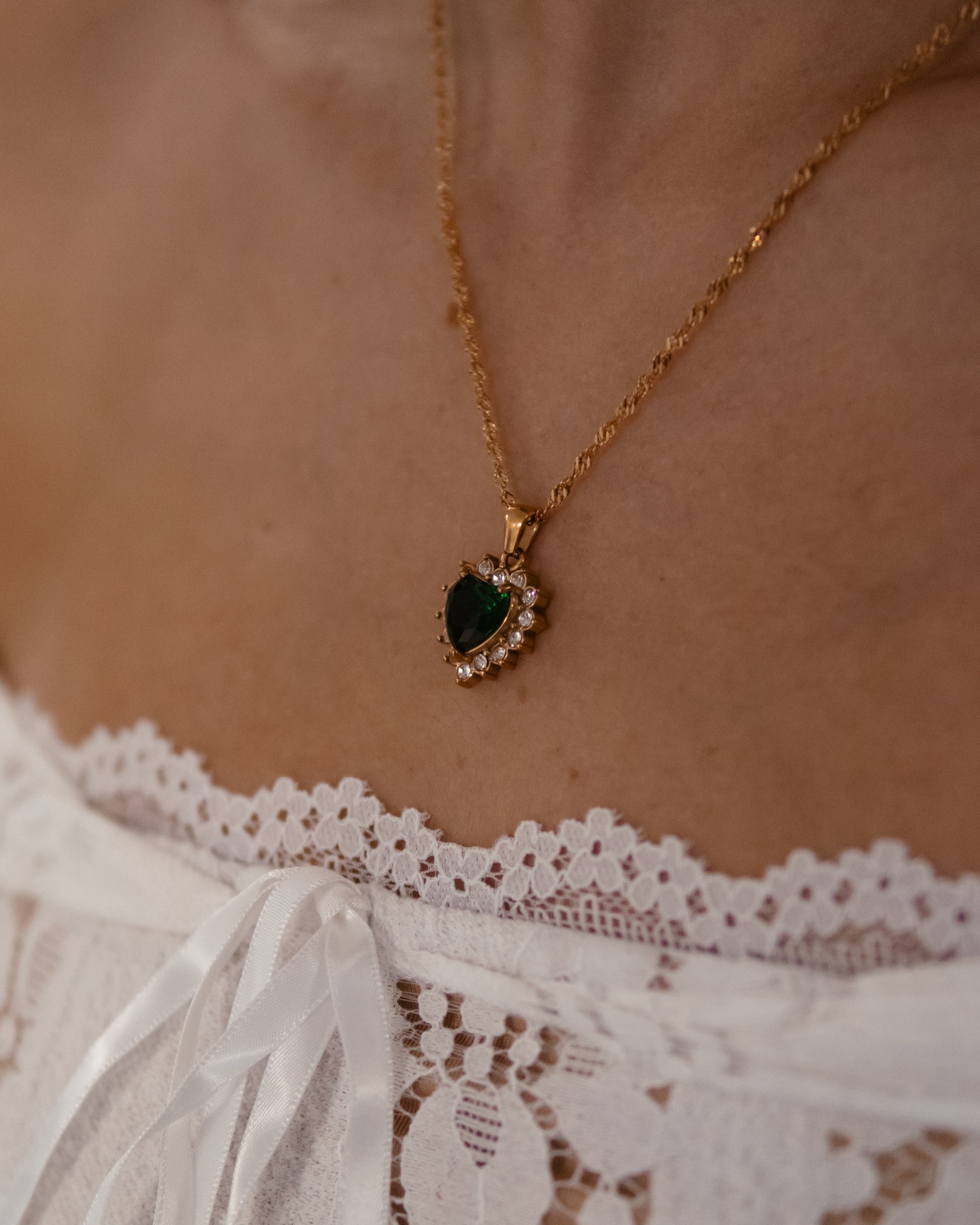 Colar dourado com pendente em gota verde e cristais em roupa branca de renda