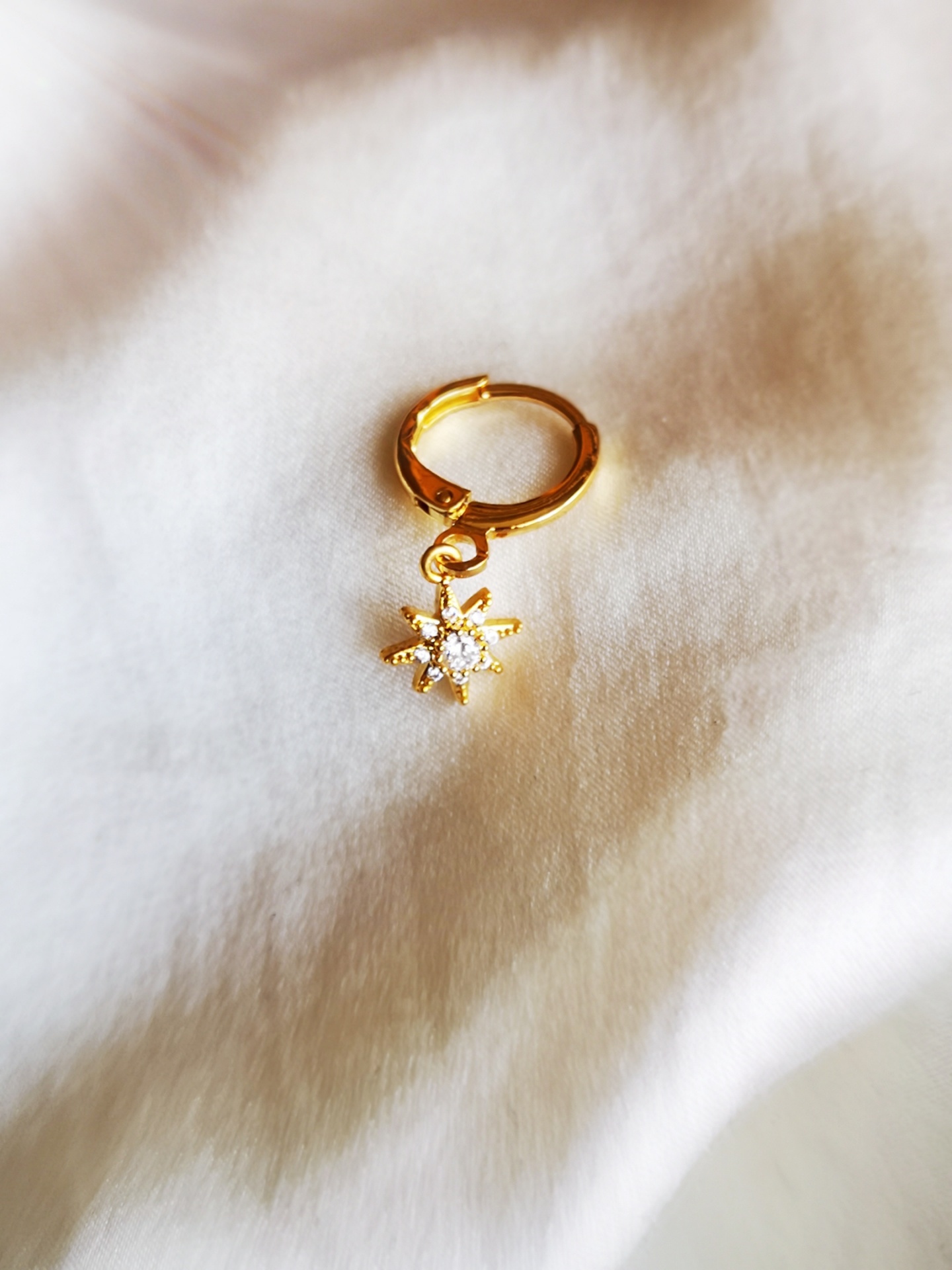 Brinco dourado com pendente floco de neve sobre tecido branco