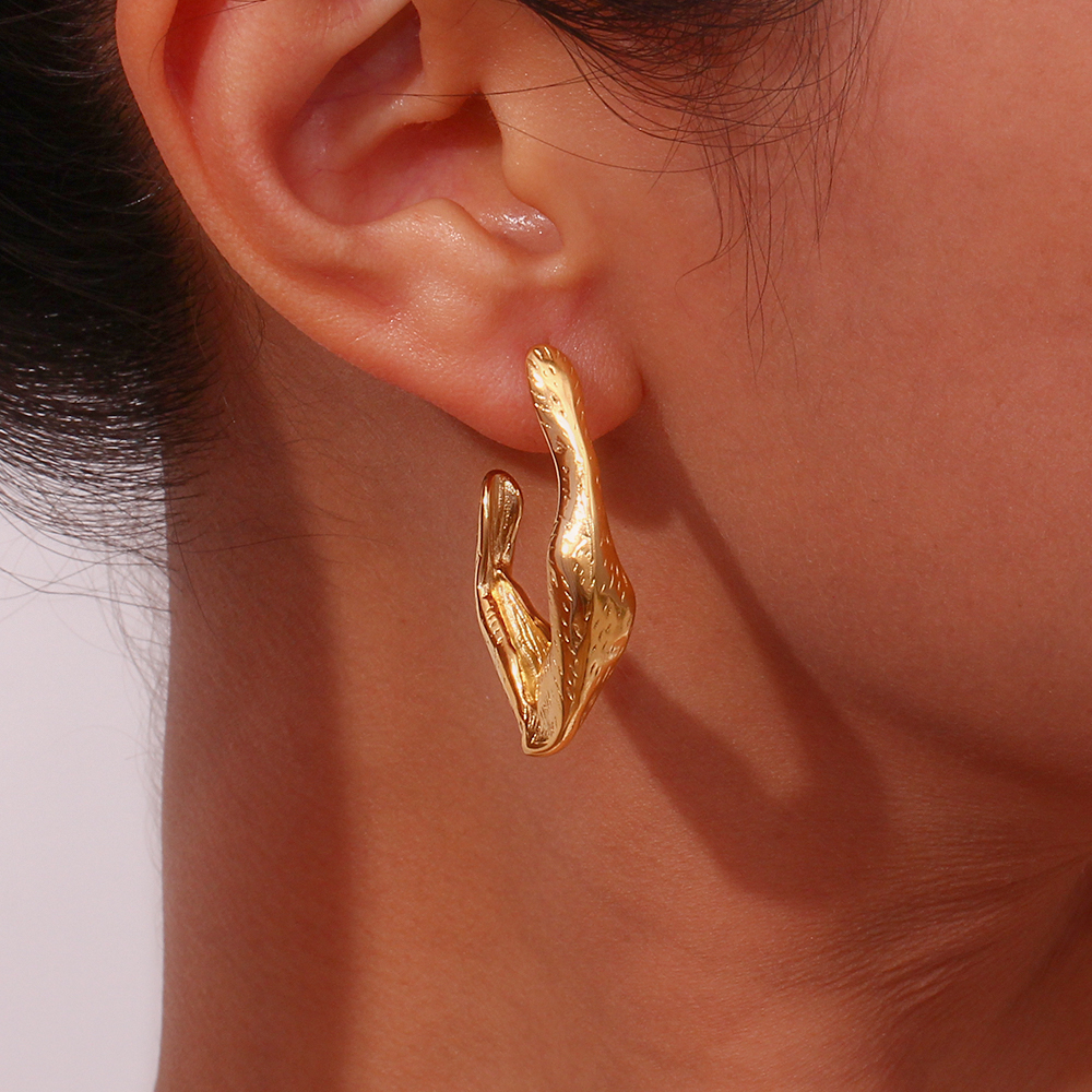 Brinco dourado com textura orgânica numa orelha feminina.