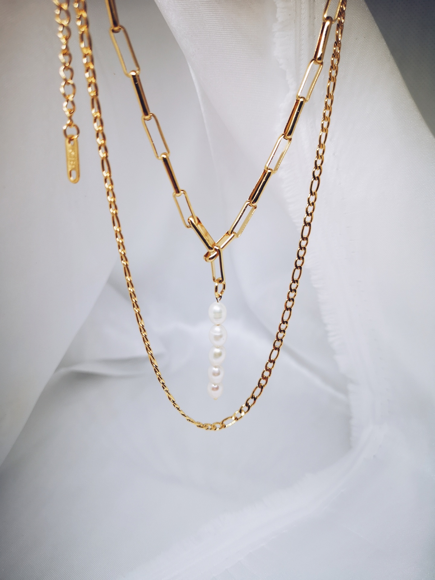 Três colares dourados com diferentes tipos de elos e um pendente de pérolas sobre fundo branco