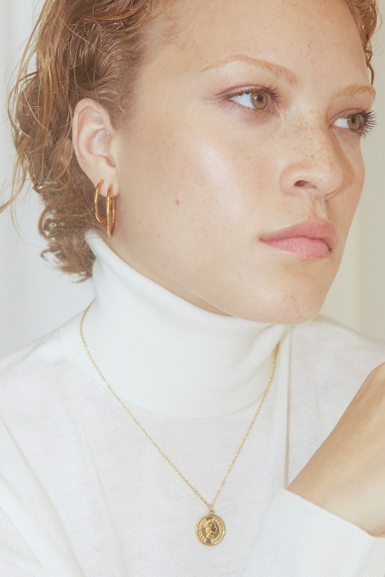 Mulher com brincos dourados em aro e colar dourado com pendente redondo