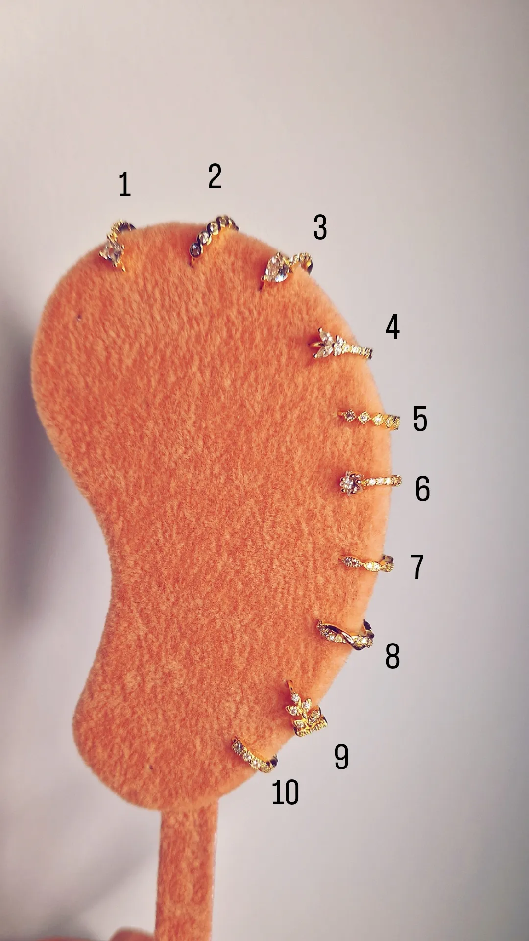 Dez brincos dourados com pedras sobre base alaranjada felpuda em forma de orelha