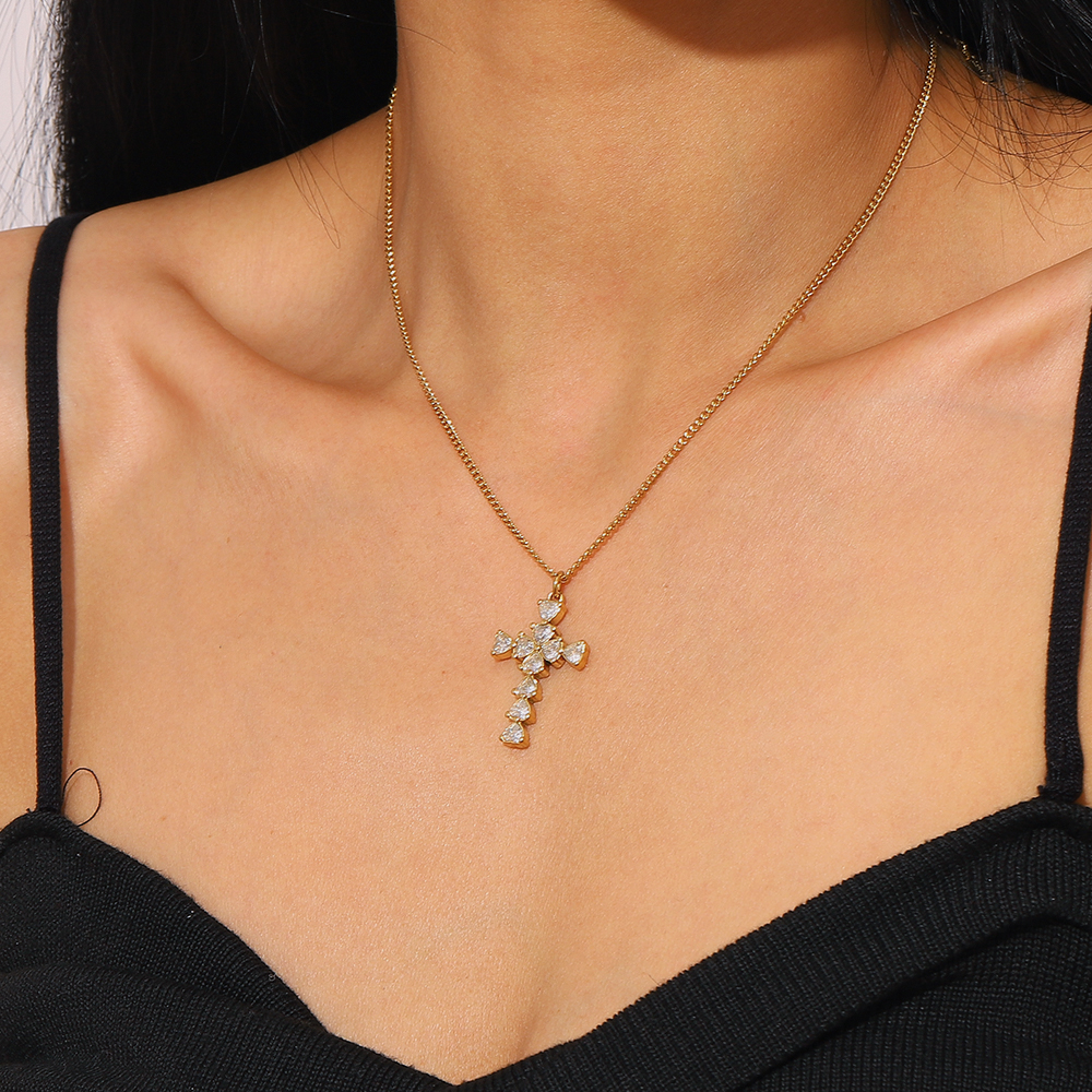 Colar dourado com cruz de pedras brilhantes no pescoço de mulher com vestido preto.