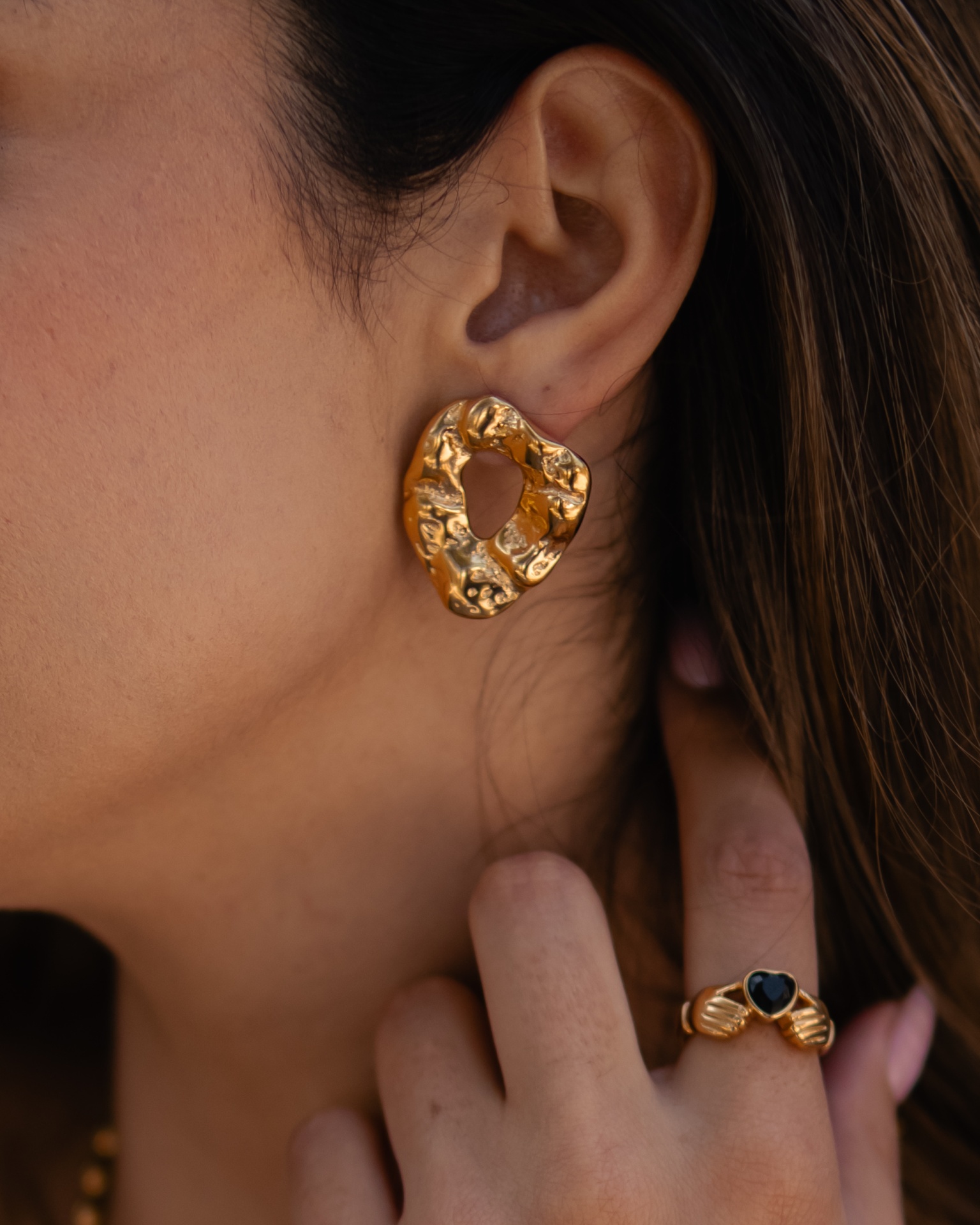 Brinco dourado de formato irregular e anel dourado com pedra preta em formato de coração