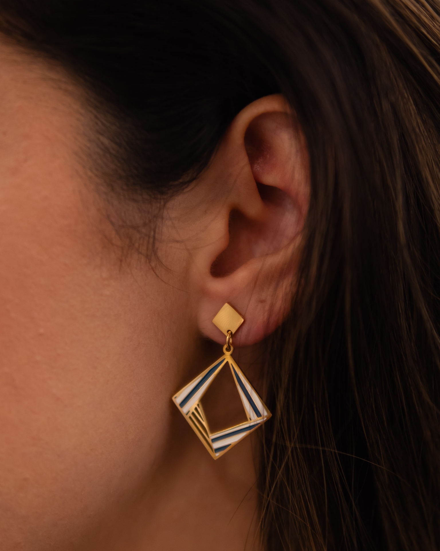 Brinco dourado geométrico com detalhes coloridos usado numa orelha
