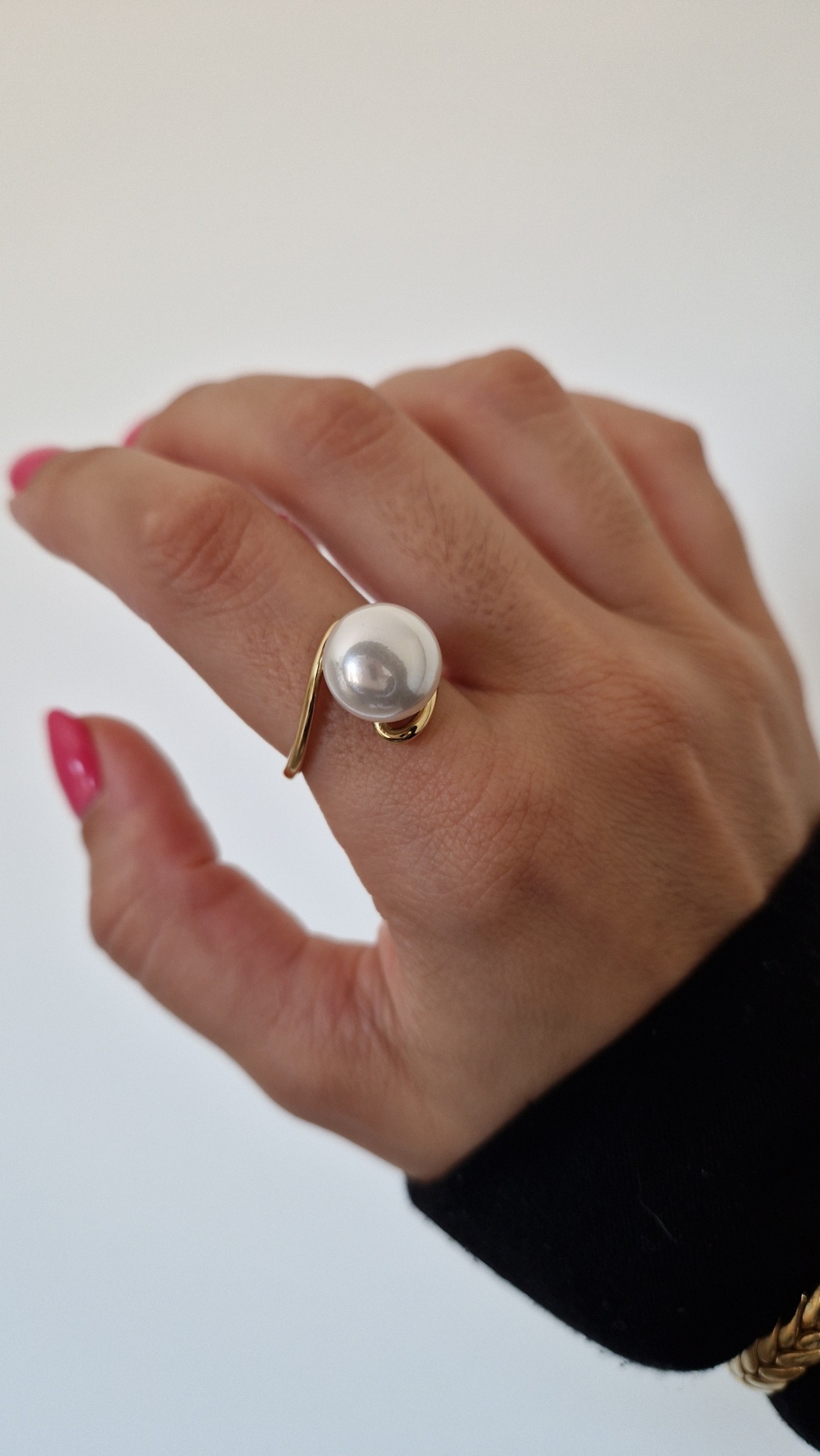 Anel dourado com pérola grande numa mão com unhas cor de rosa