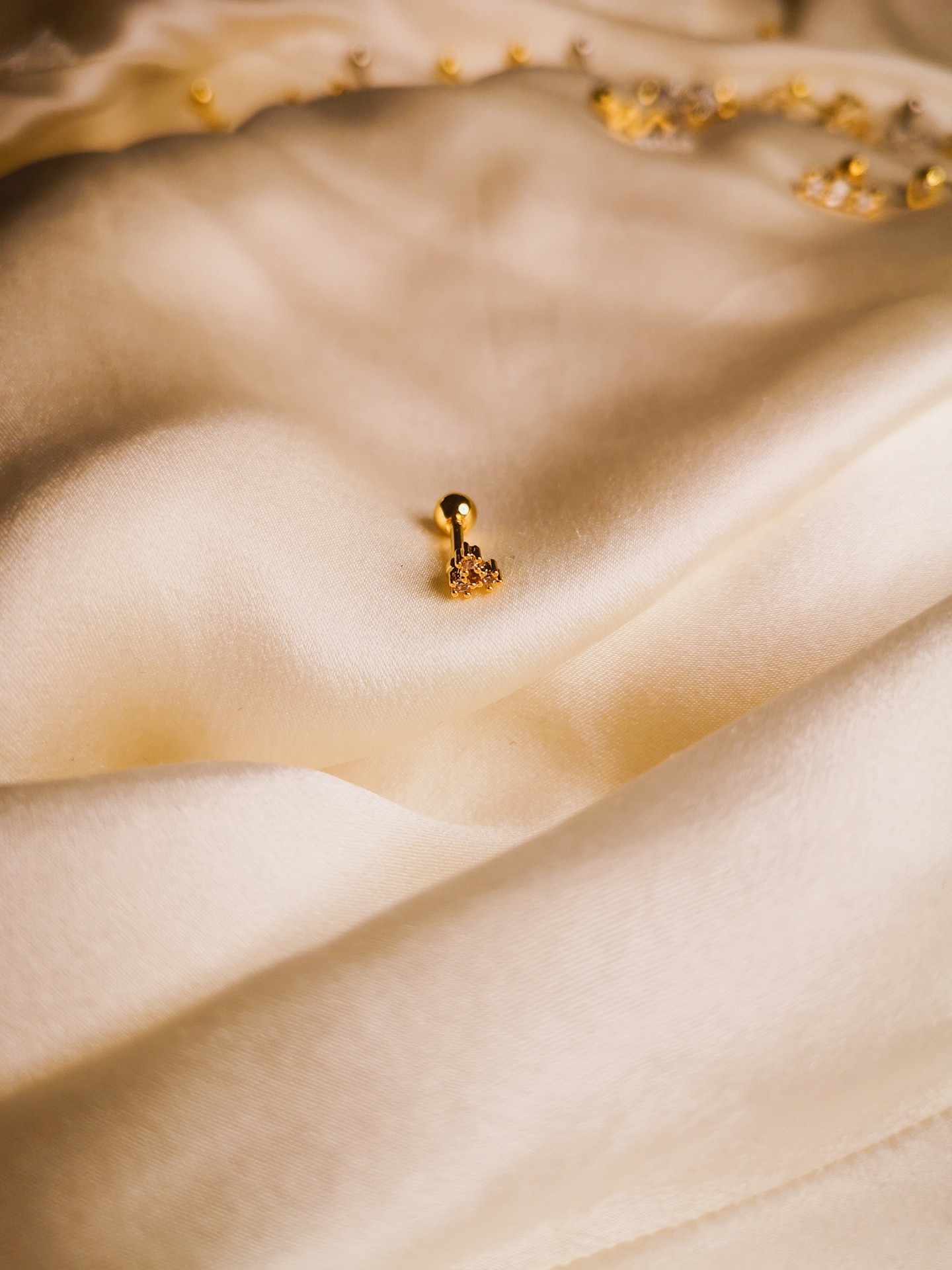 Brinco dourado pequeno em tecido branco com outros brincos ao fundo