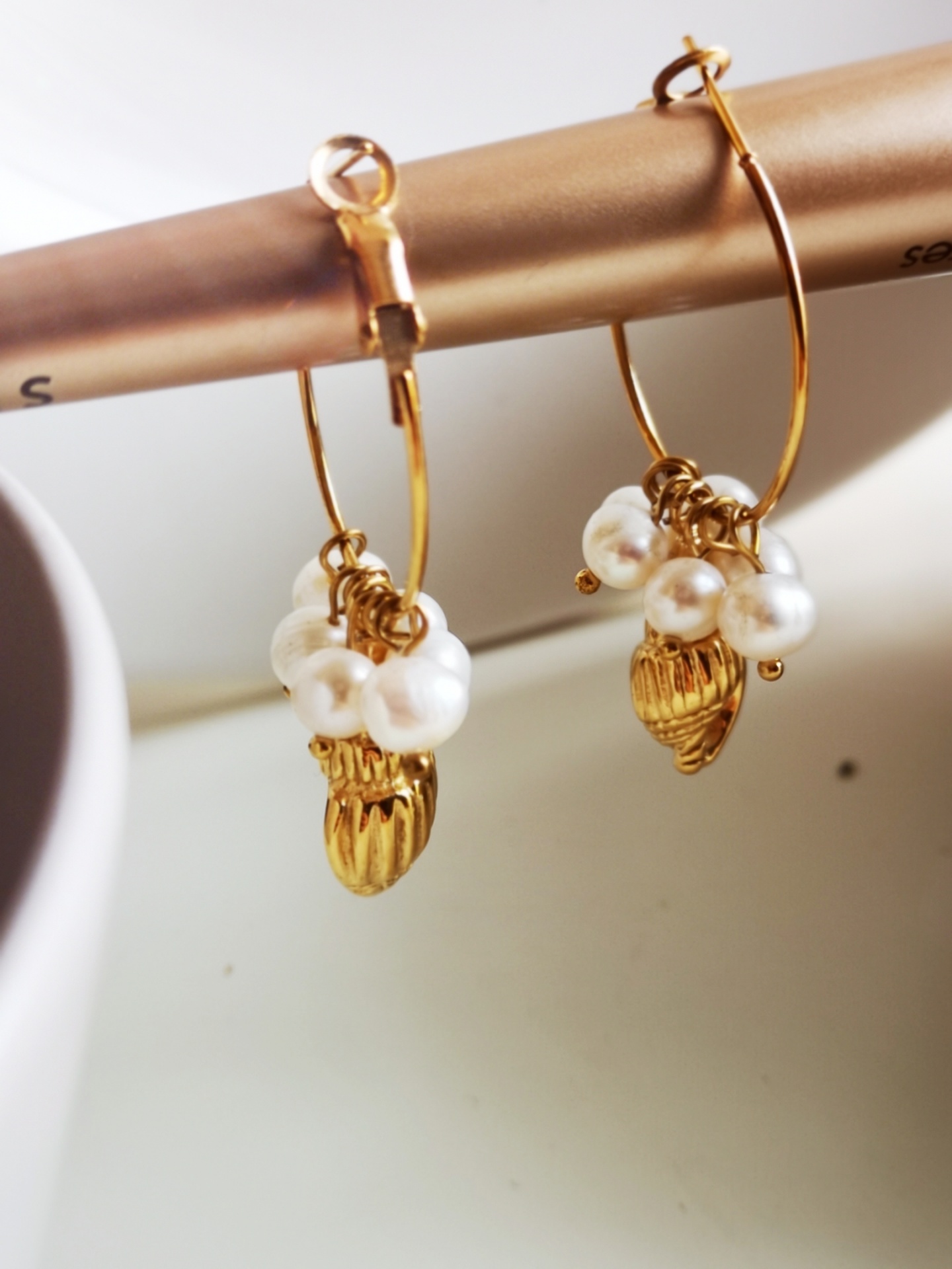 Brincos dourados com pérolas e pingentes pendurados.