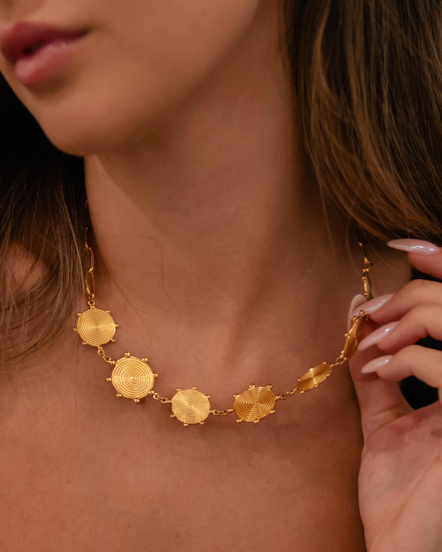 Colar dourado com medalhões redondos texturizados no pescoço de mulher