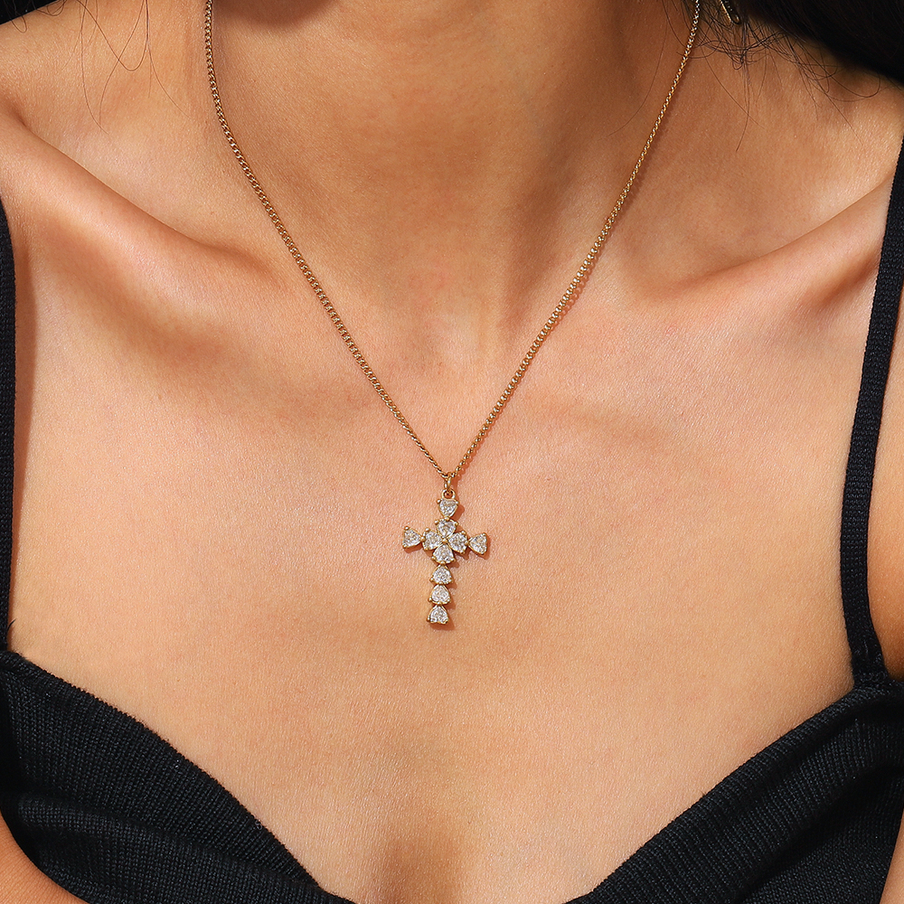 Colar dourado com pendente de cruz e pedras brilhantes em pescoço feminino com vestido preto.