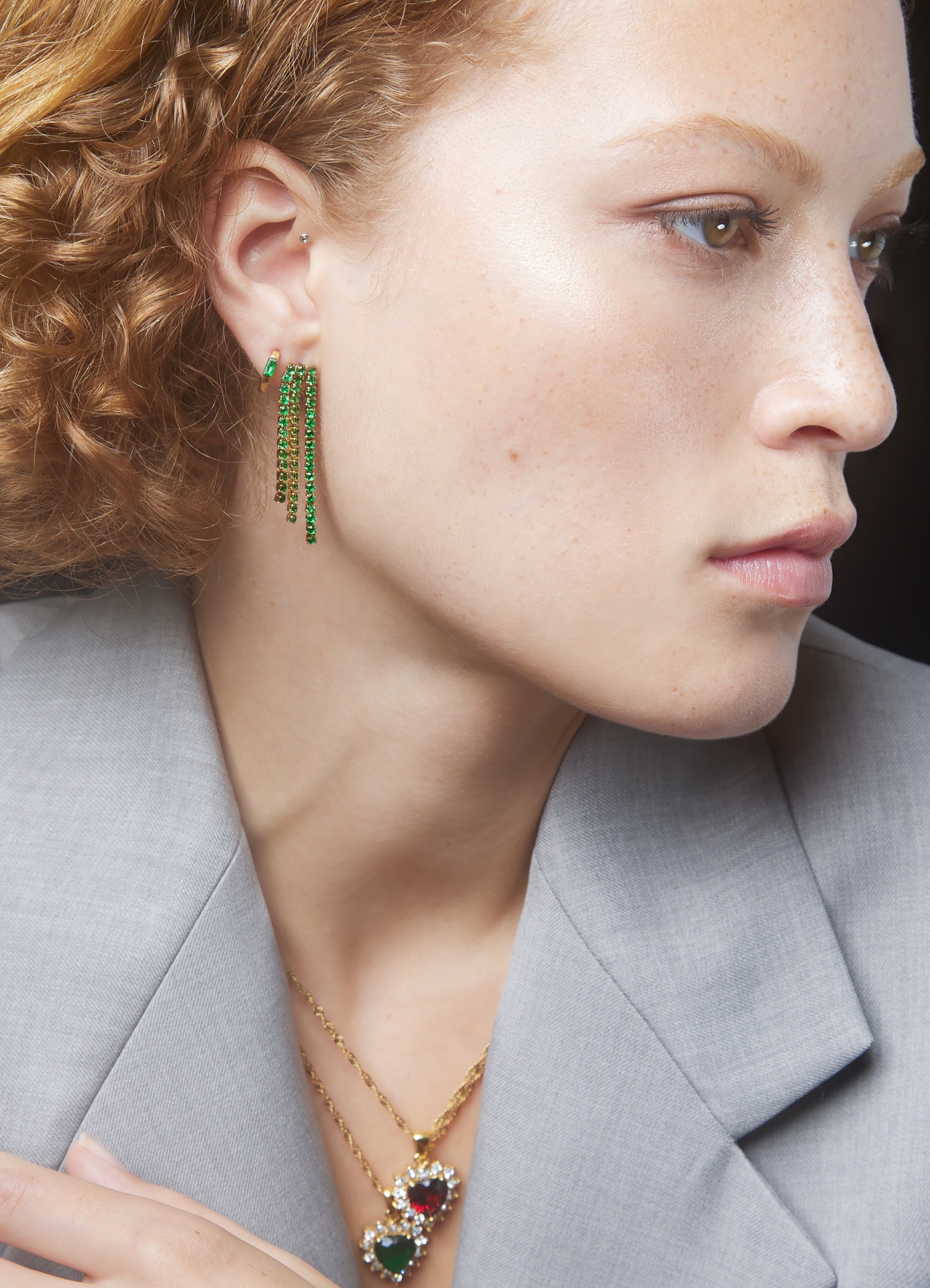 Brincos pendentes verdes e dourados e colares dourados com pendentes coloridos usados por mulher com casaco cinza