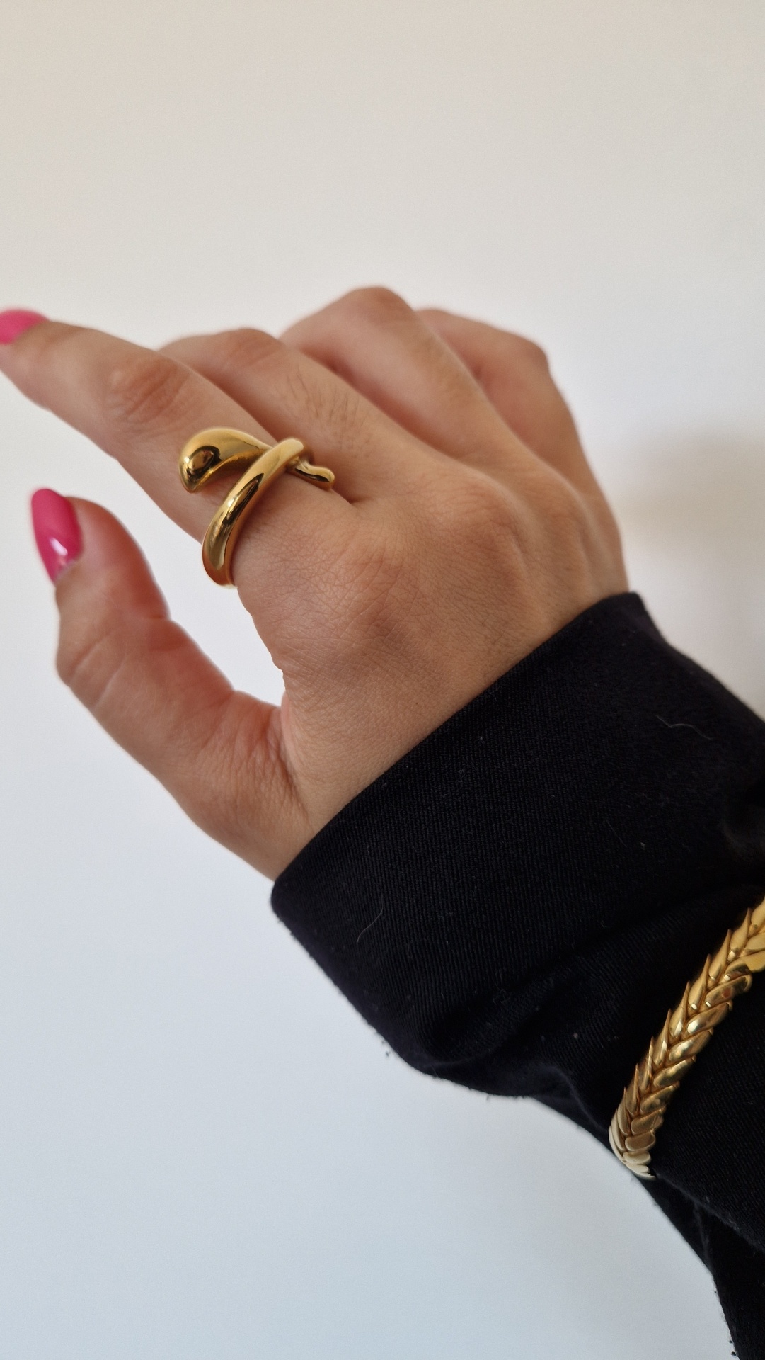 Mão com anel dourado em forma de cobra e pulseira dourada, unhas rosa e manga preta