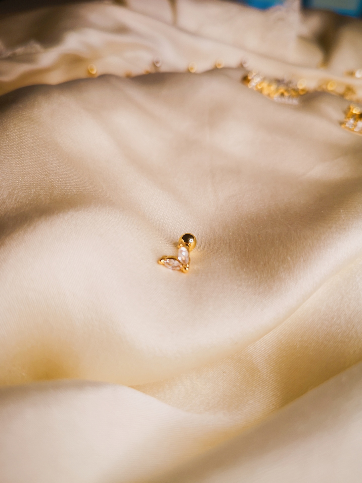 Brincos pequenos dourados com cristais sobre tecido creme