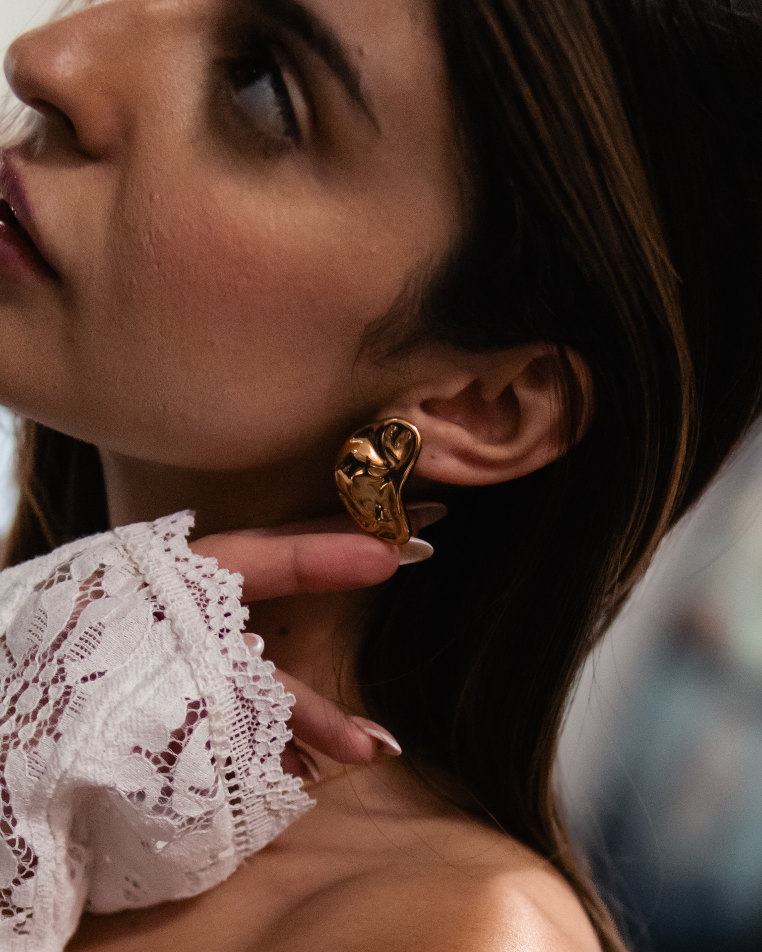 Brincos dourados com design irregular em mulher com blusa de renda branca