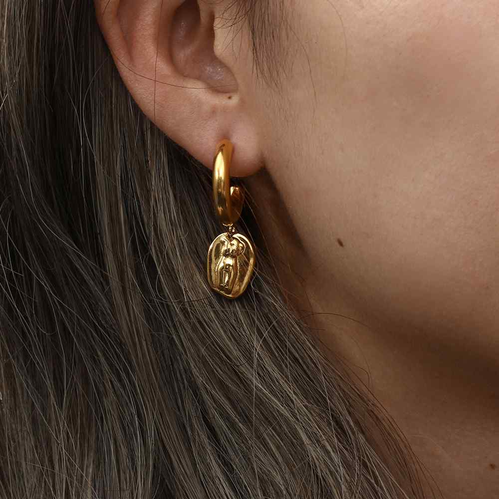 Brinco dourado com medalha pendurada em orelha