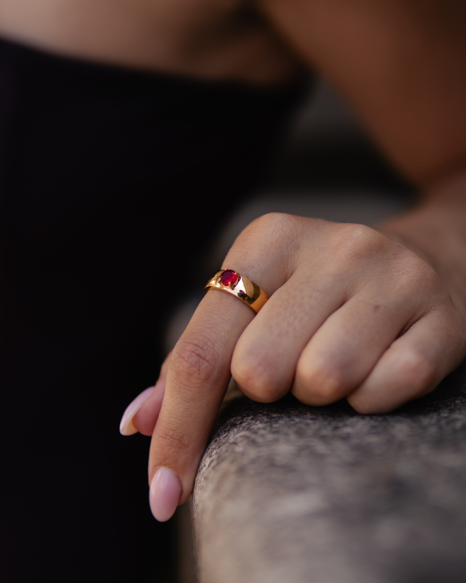 Anel dourado com pedra vermelha em mão sobre superfície de pedra