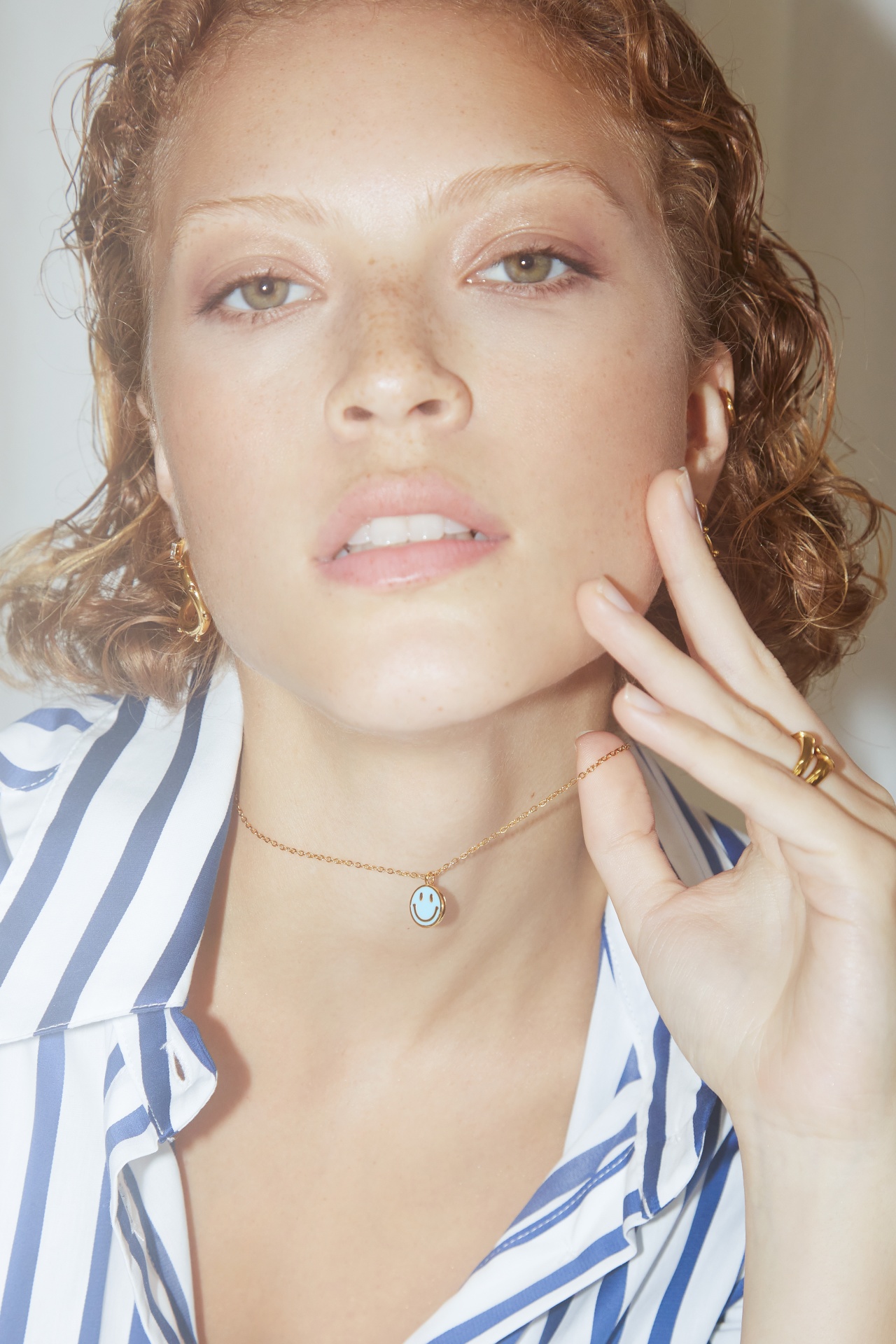 Colar dourado com pendente redondo azul claro e branco com mulher de camisa riscada azul e branca