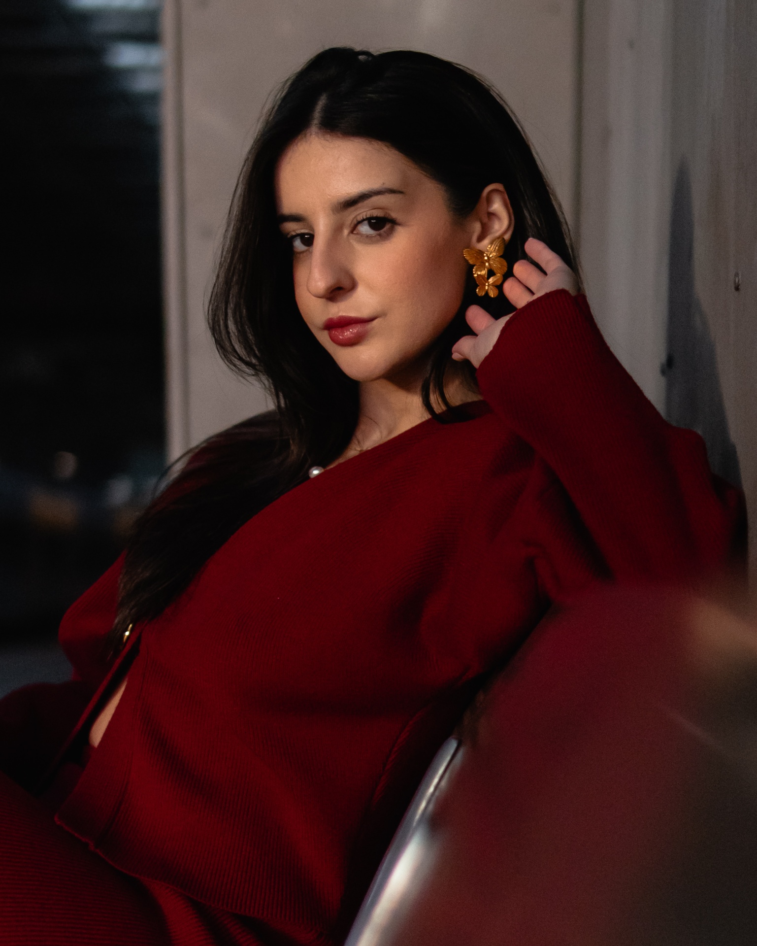 Mulher com casaco vermelho e brincos dourados em ambiente interno