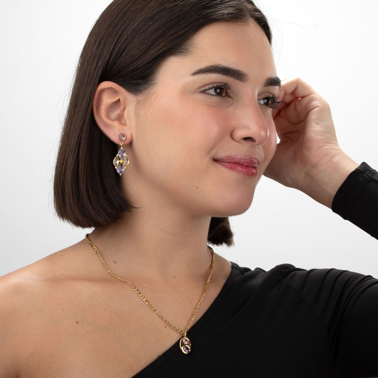 Mulher com colar e brincos dourados com pedras roxas, usando blusa preta
