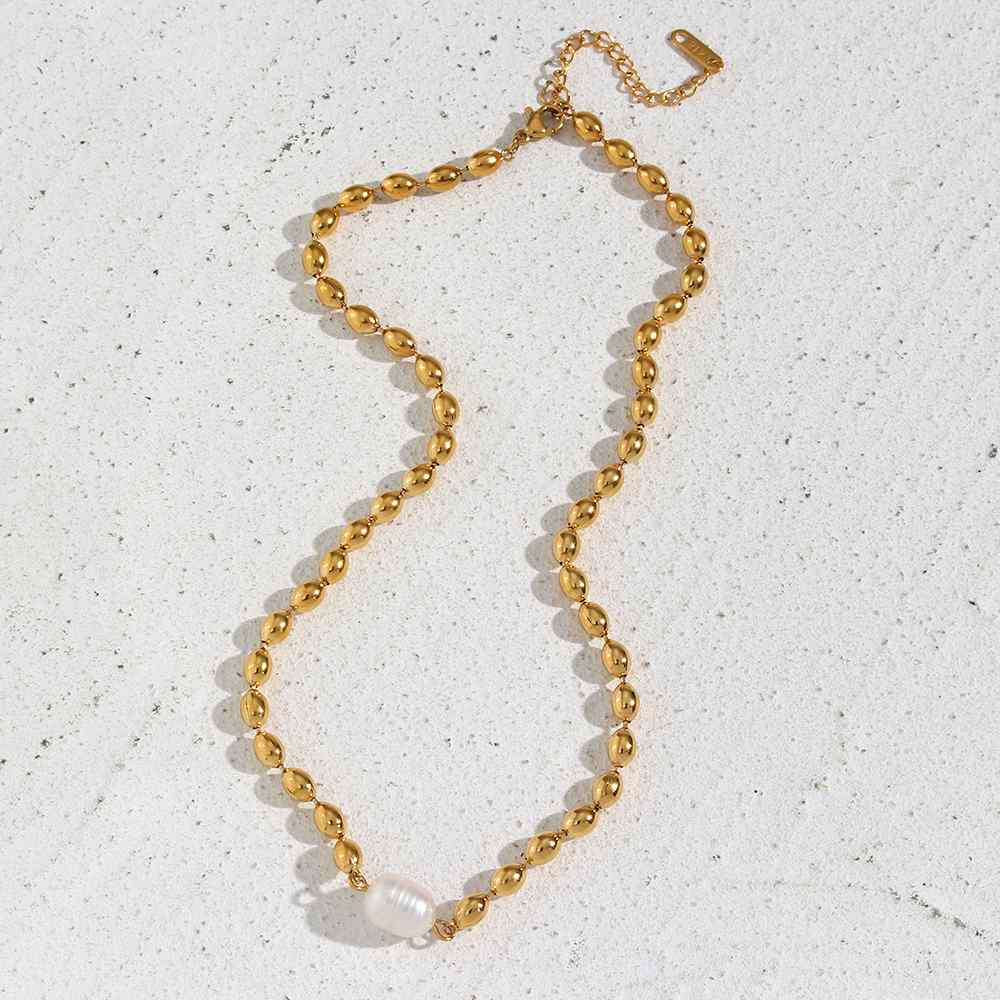 Colar dourado com pérola branca numa superfície clara texturada