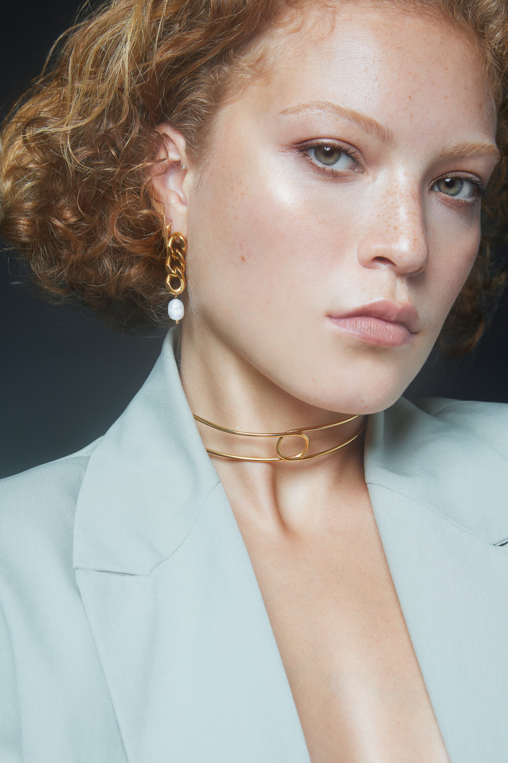 mulher com brinco de corrente dourada e colar dourado usando blazer cinza claro