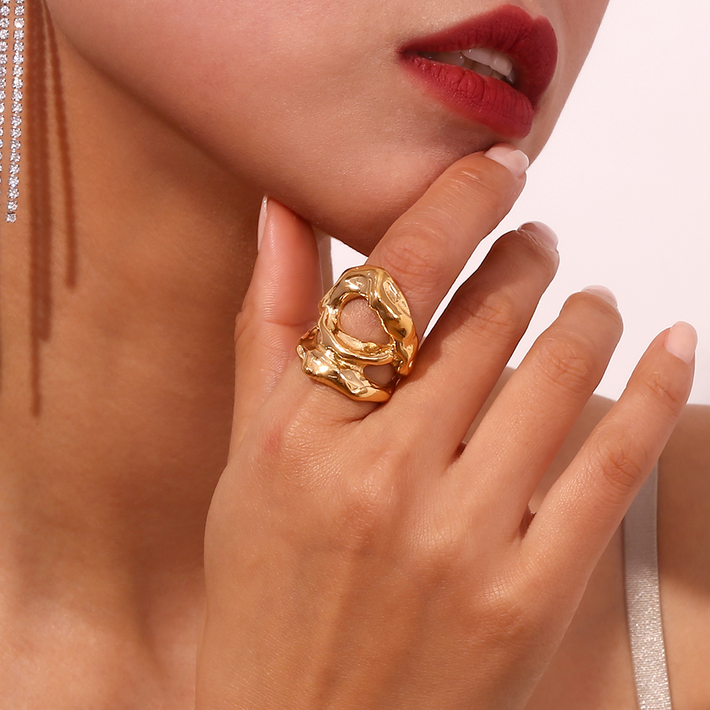 Anel dourado orgânico numa mão feminina com batom vermelho e brinco pendente