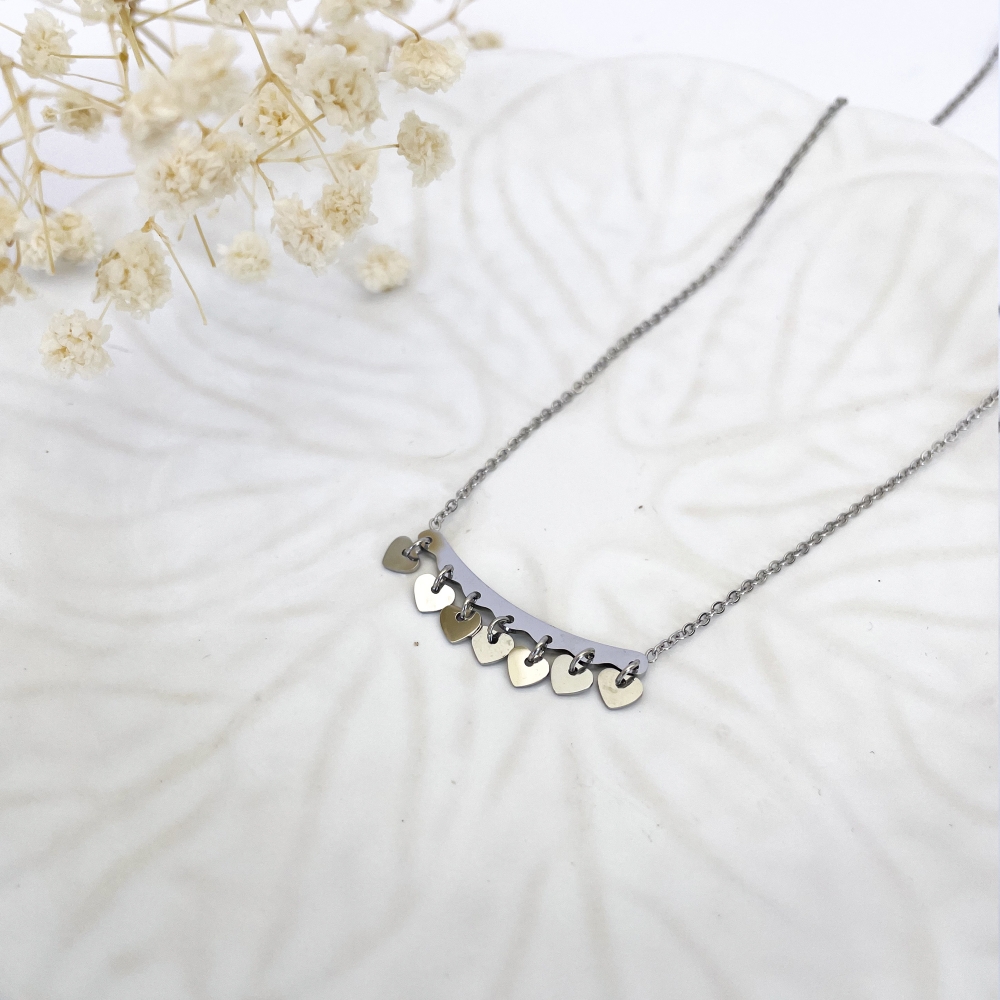 Colar em aço com pendentes de coração sobre prato branco com flores secas