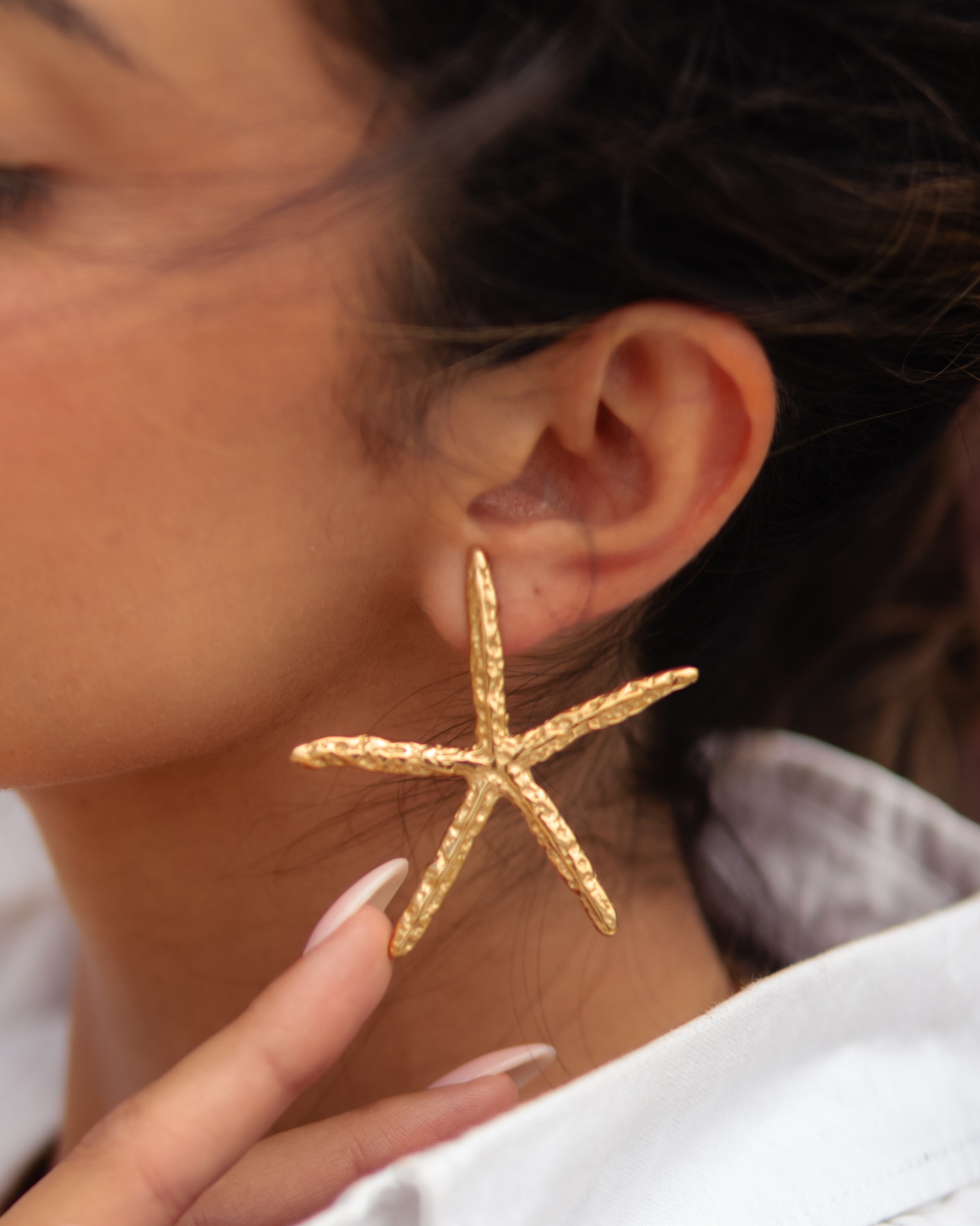 Brinco dourado em forma de estrela do mar na orelha de uma mulher
