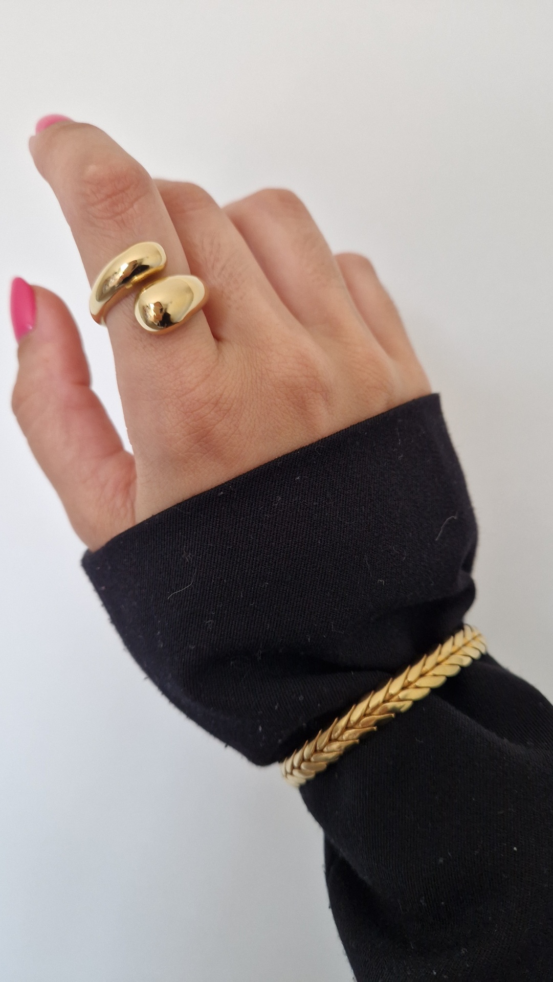Mão feminina com anel dourado e pulseira dourada com manga preta